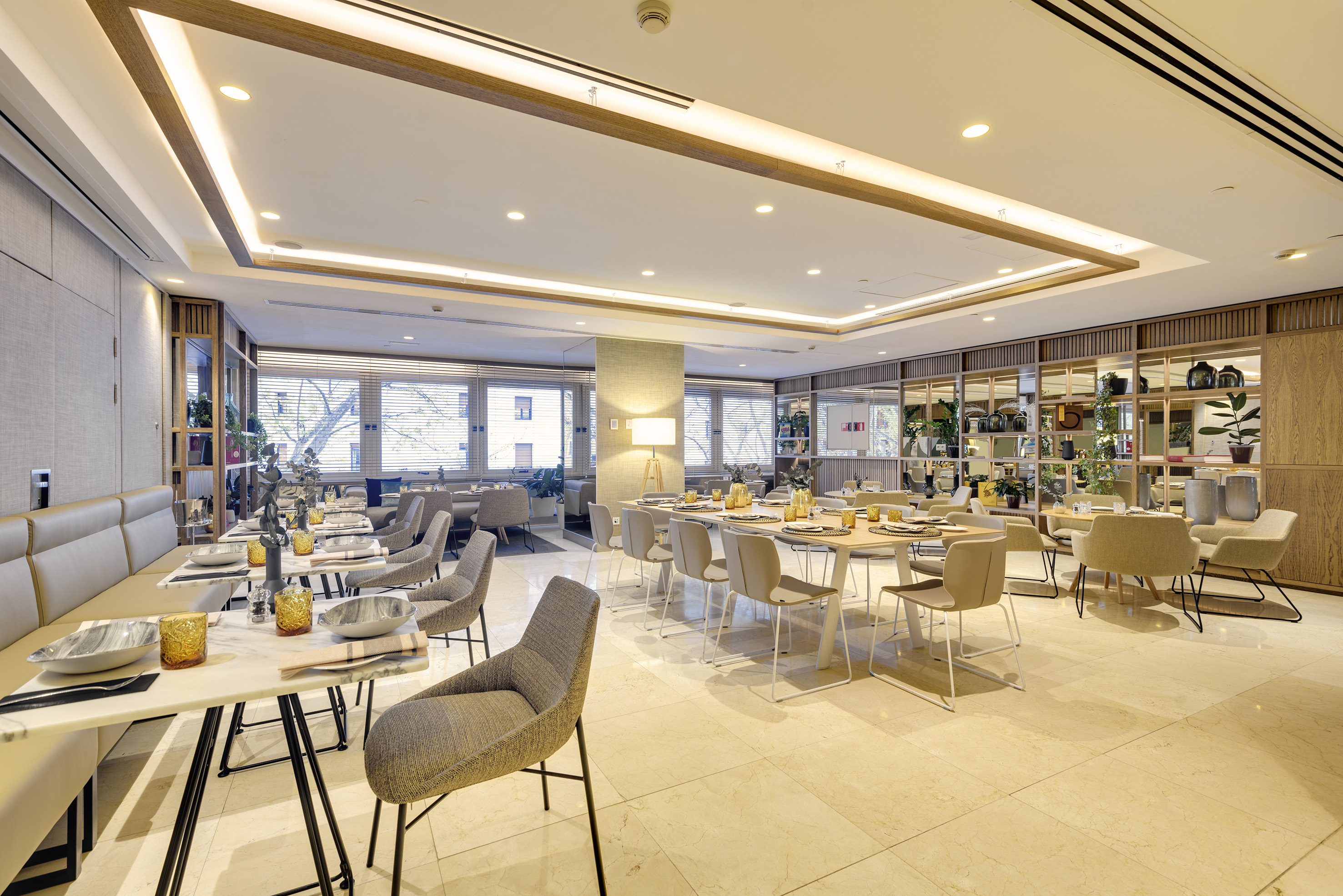 Modern restaurant dining room with elegant set tables, chairs, and warm lighting.