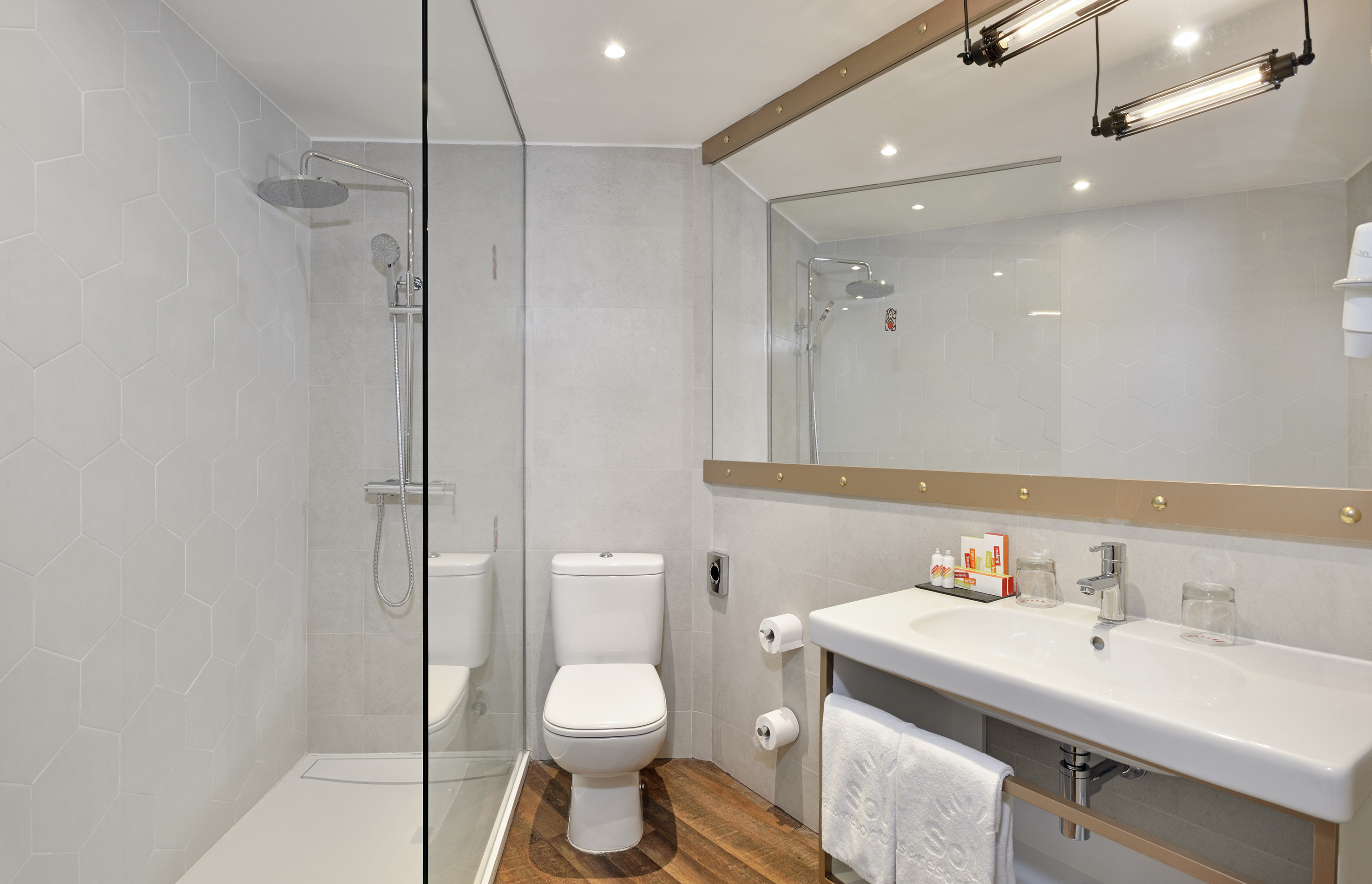 Modern hotel bathroom: glass shower, toilet, sink, hexagon tiles.