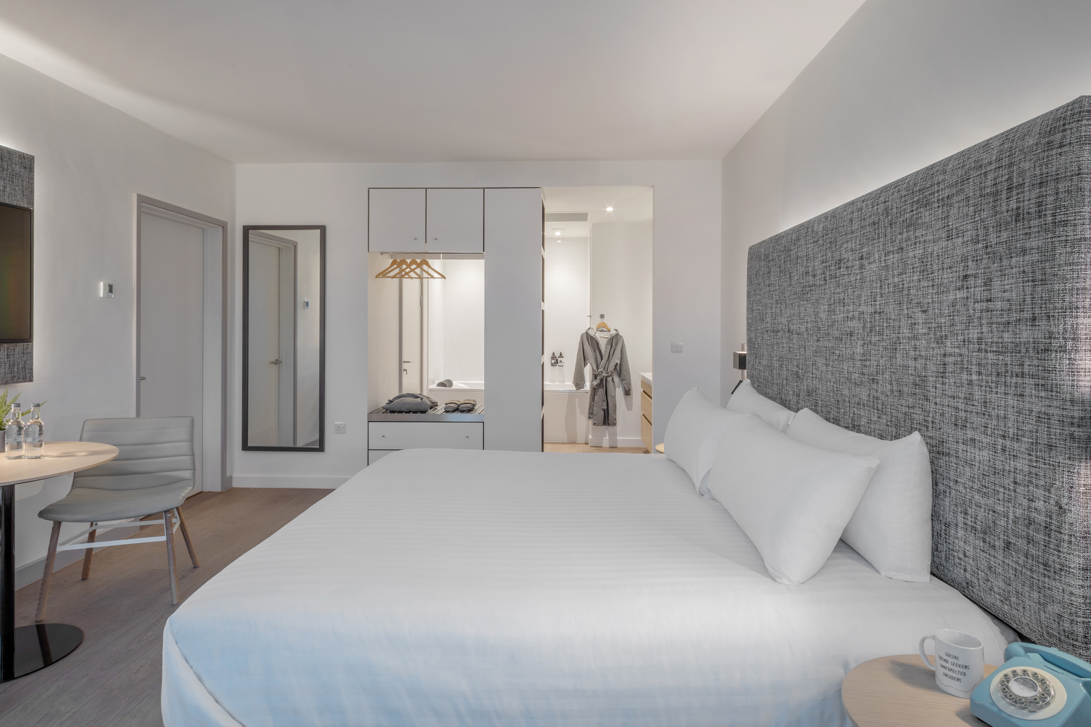 Modern hotel room with king bed, textured headboard, and open-plan bathroom.