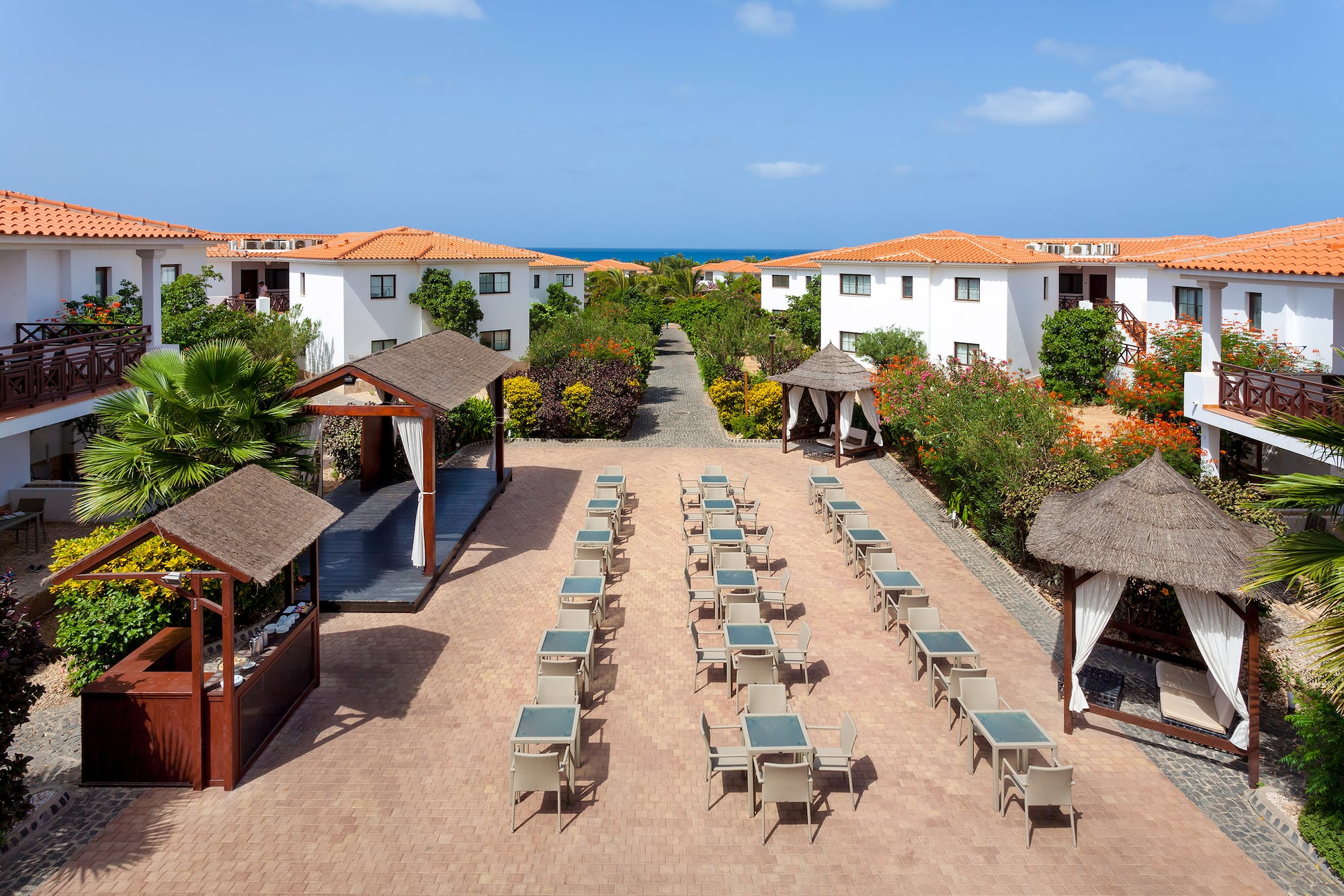 a group of tables and chairs in a courtyard with white buildings and blue sky
