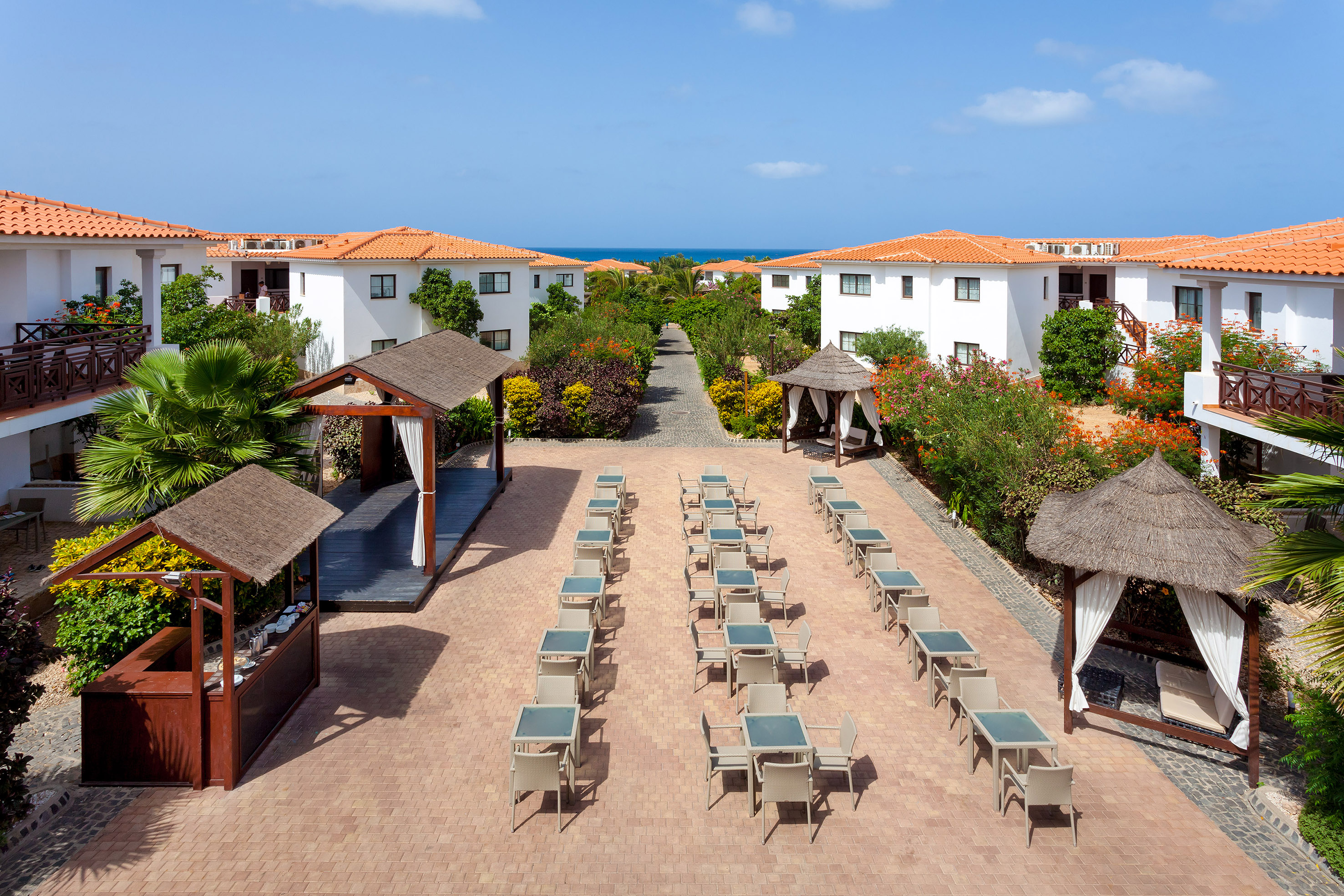 a group of tables and chairs in a courtyard with white buildings and blue sky