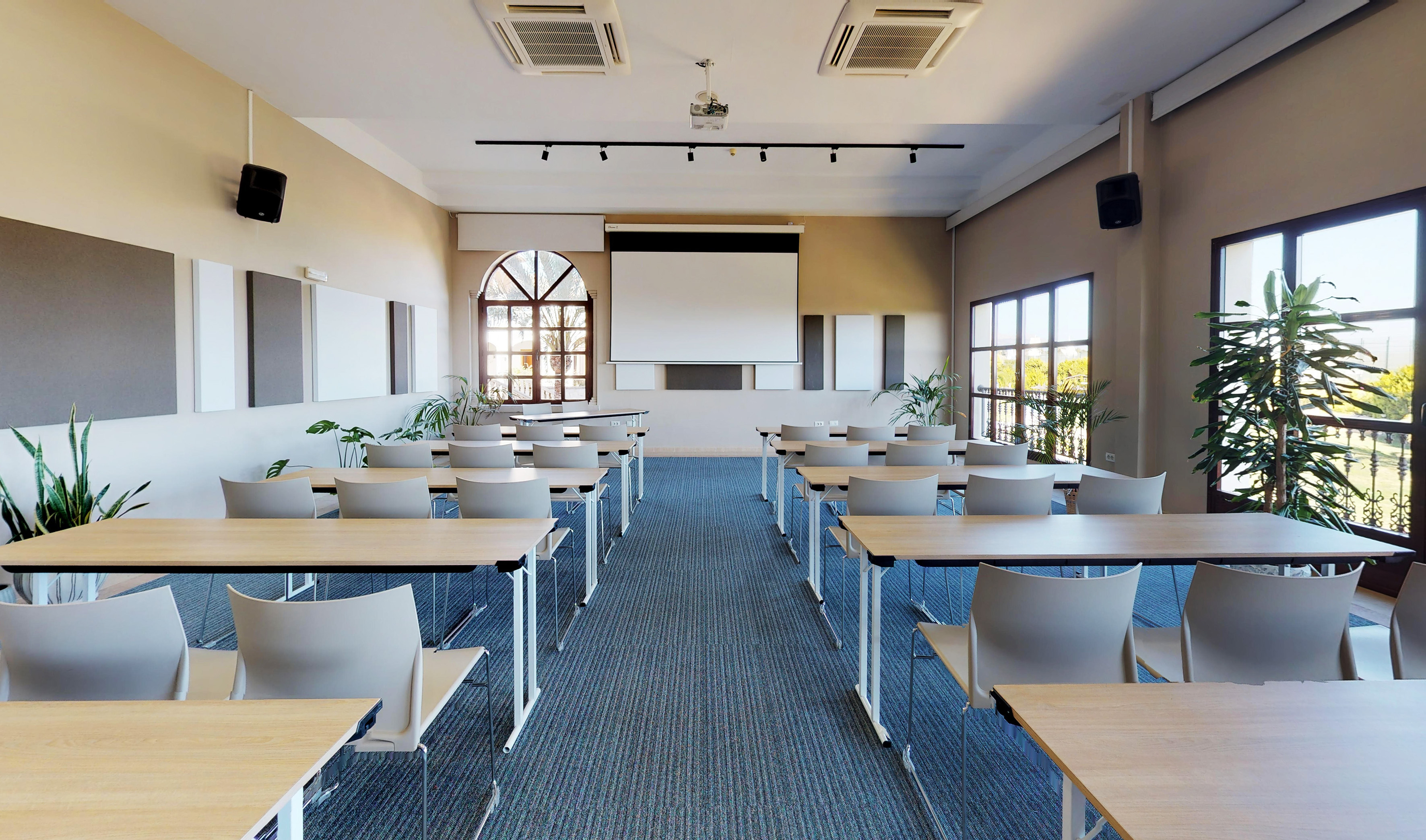 Modern training room with projector screen, tables, chairs, and windows.