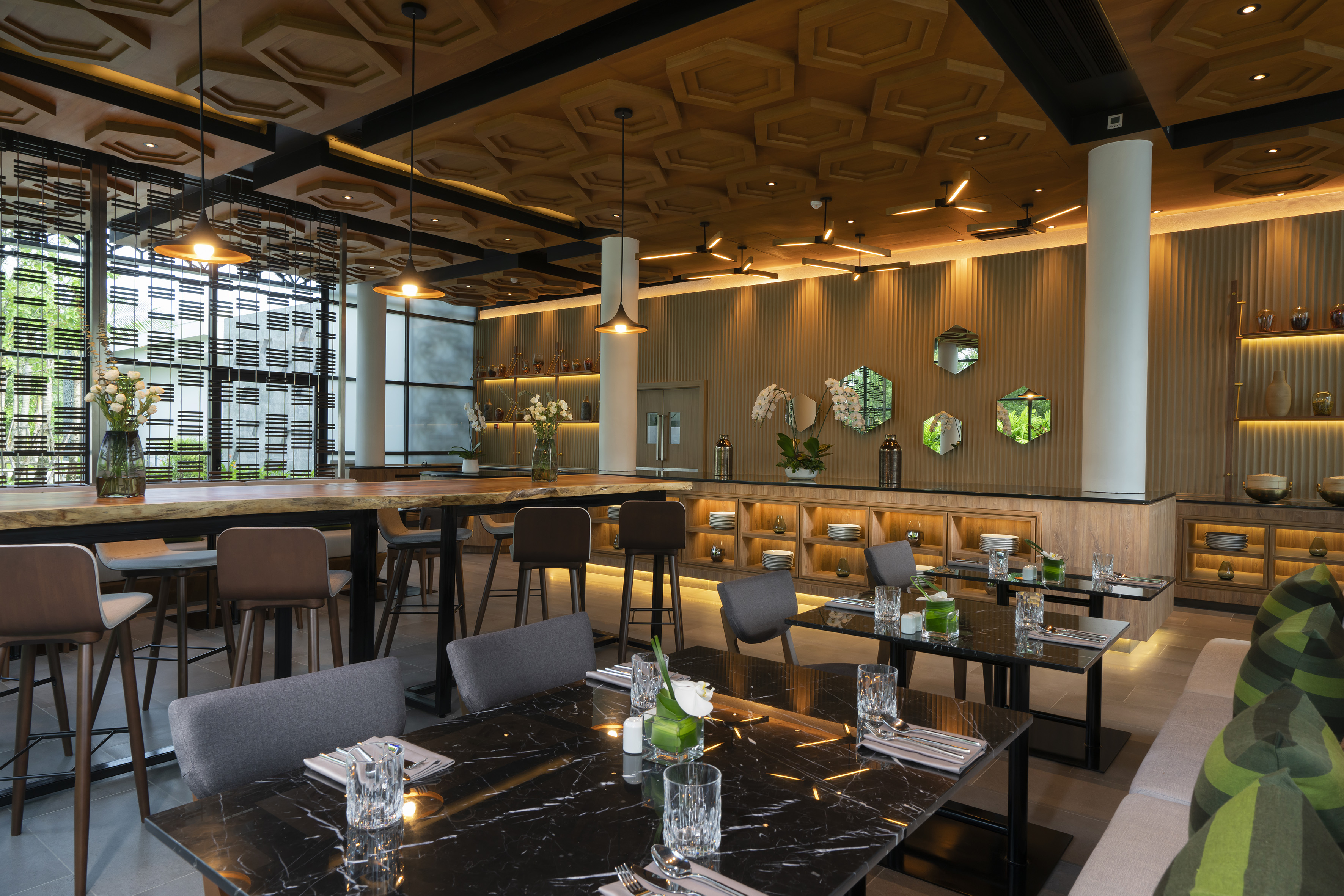 Modern restaurant with wooden ceiling, communal table, and marble dining tables.