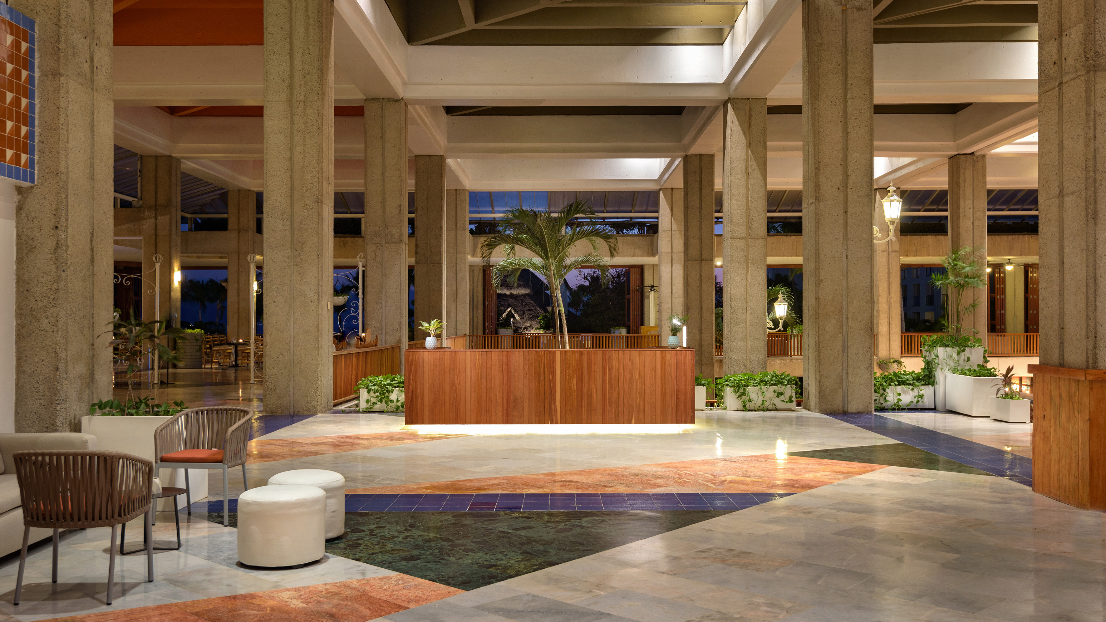 Tropical hotel lobby with concrete pillars, wooden reception, and geometric floor.