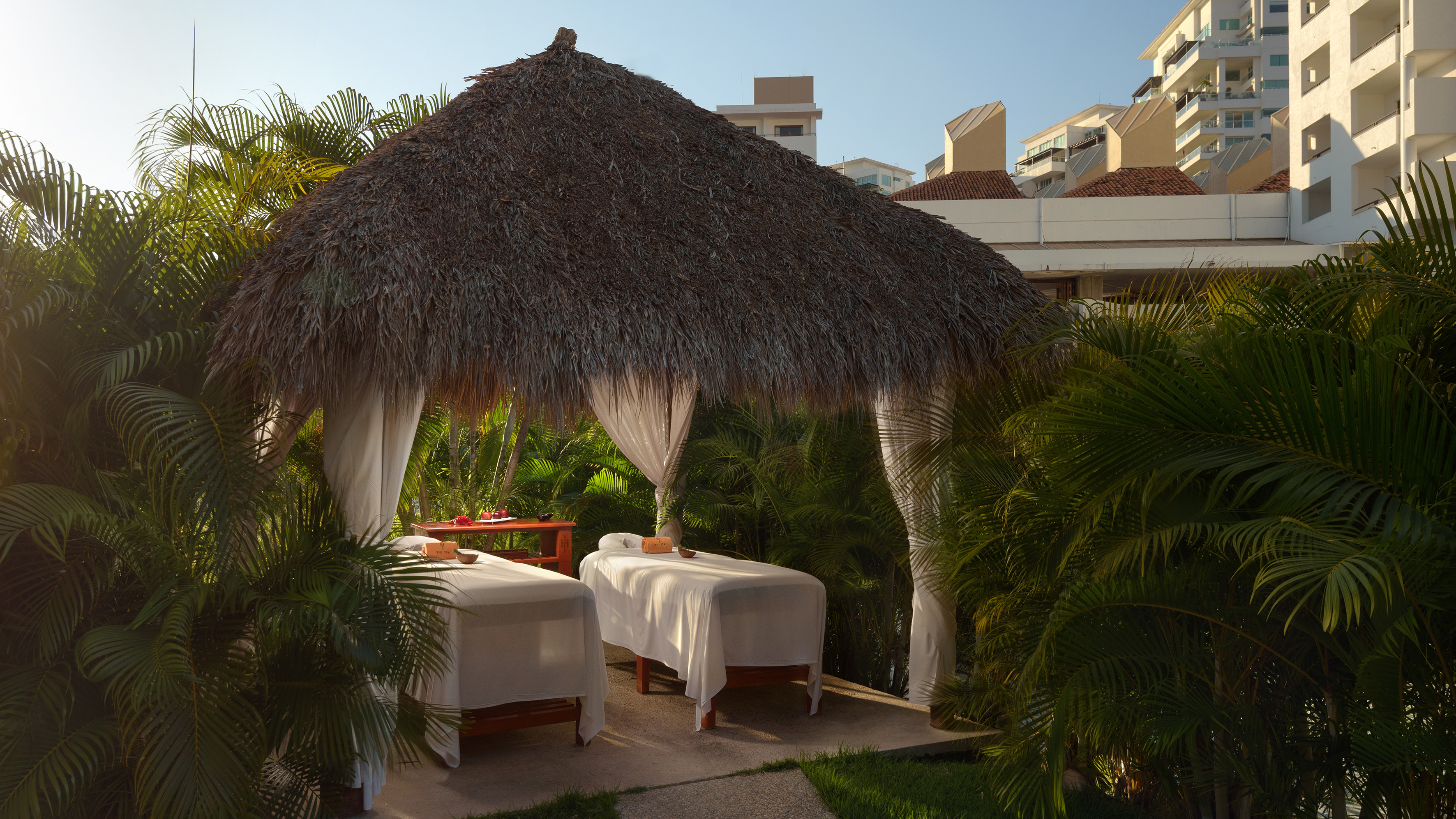 Tropical outdoor spa cabana with two massage beds and palm trees.
