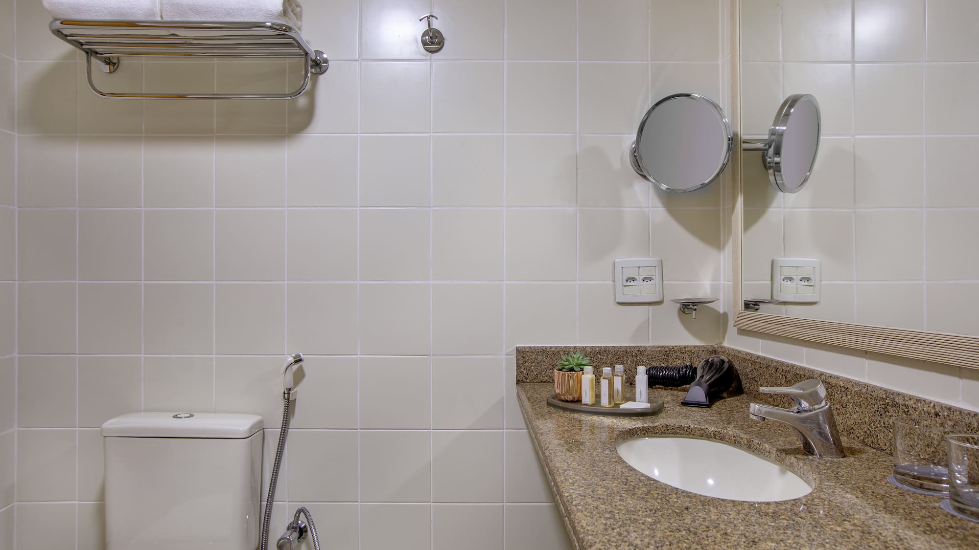 Clean hotel bathroom with toilet, granite vanity, sink, mirror, and white towels.
