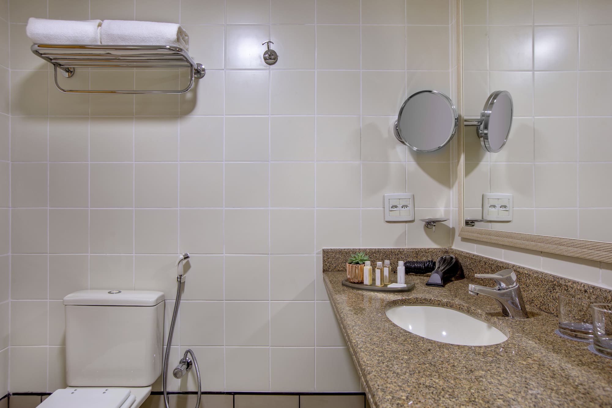 Clean hotel bathroom with toilet, granite vanity, sink, mirror, and white towels.