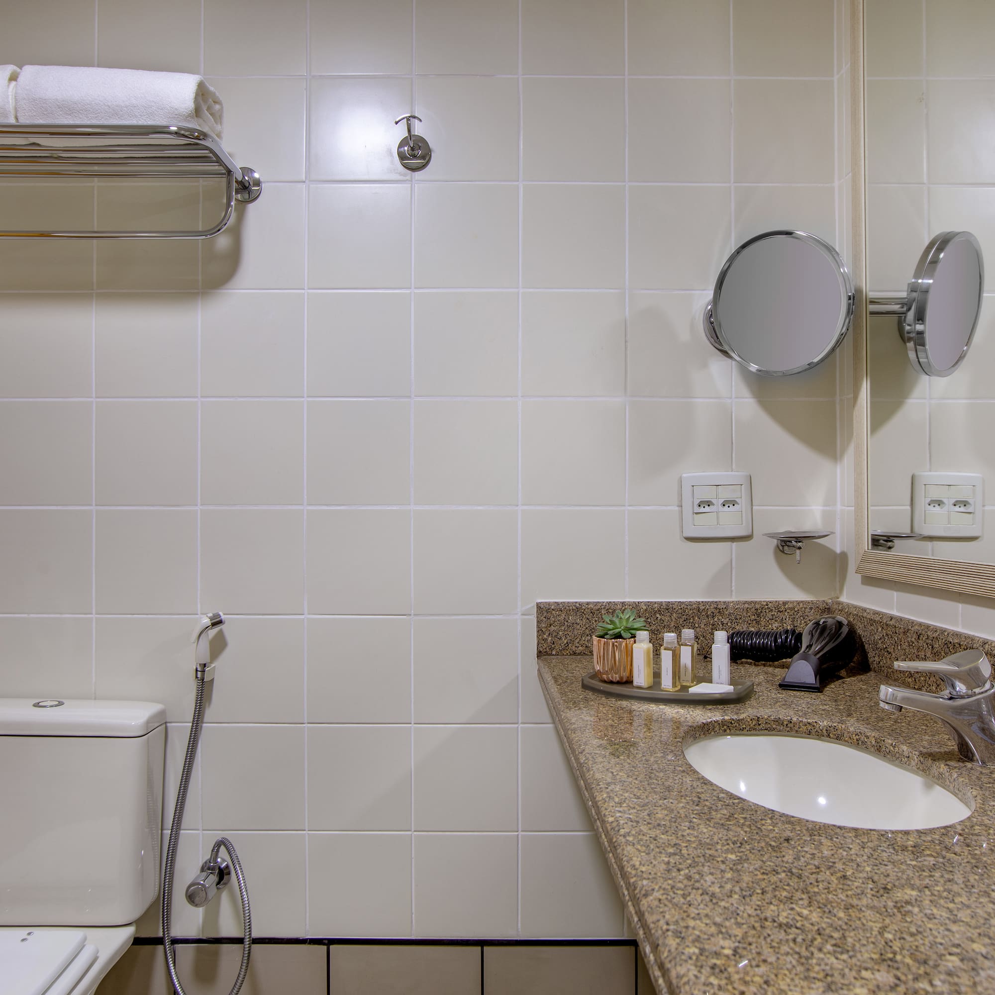 Clean hotel bathroom with toilet, granite vanity, sink, mirror, and white towels.