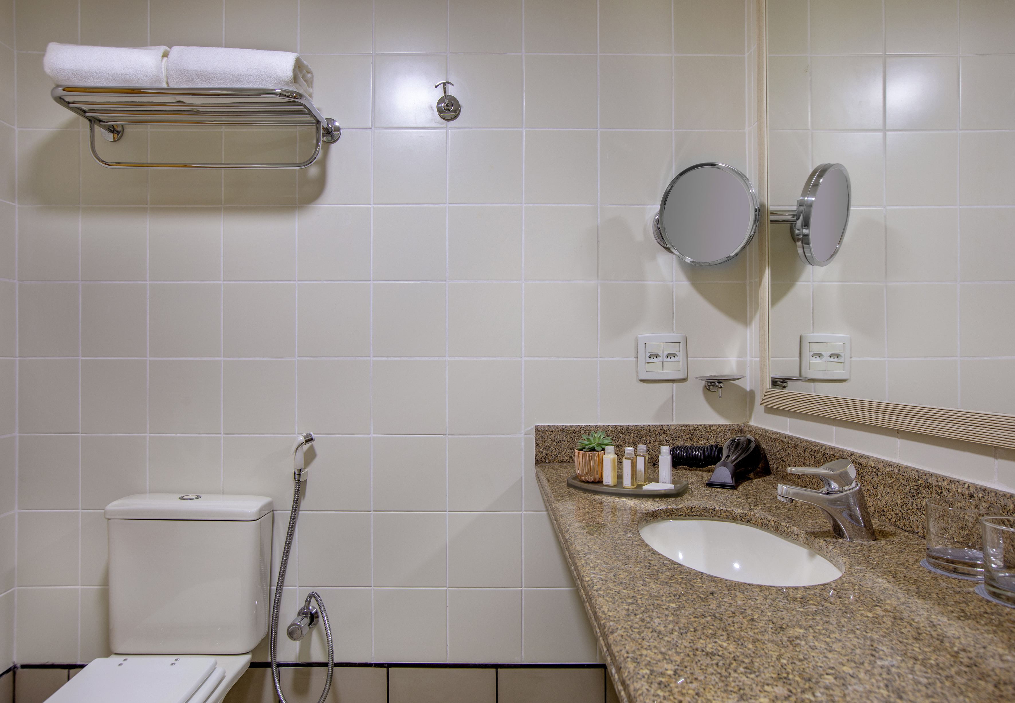 Clean hotel bathroom with toilet, granite vanity, sink, mirror, and white towels.