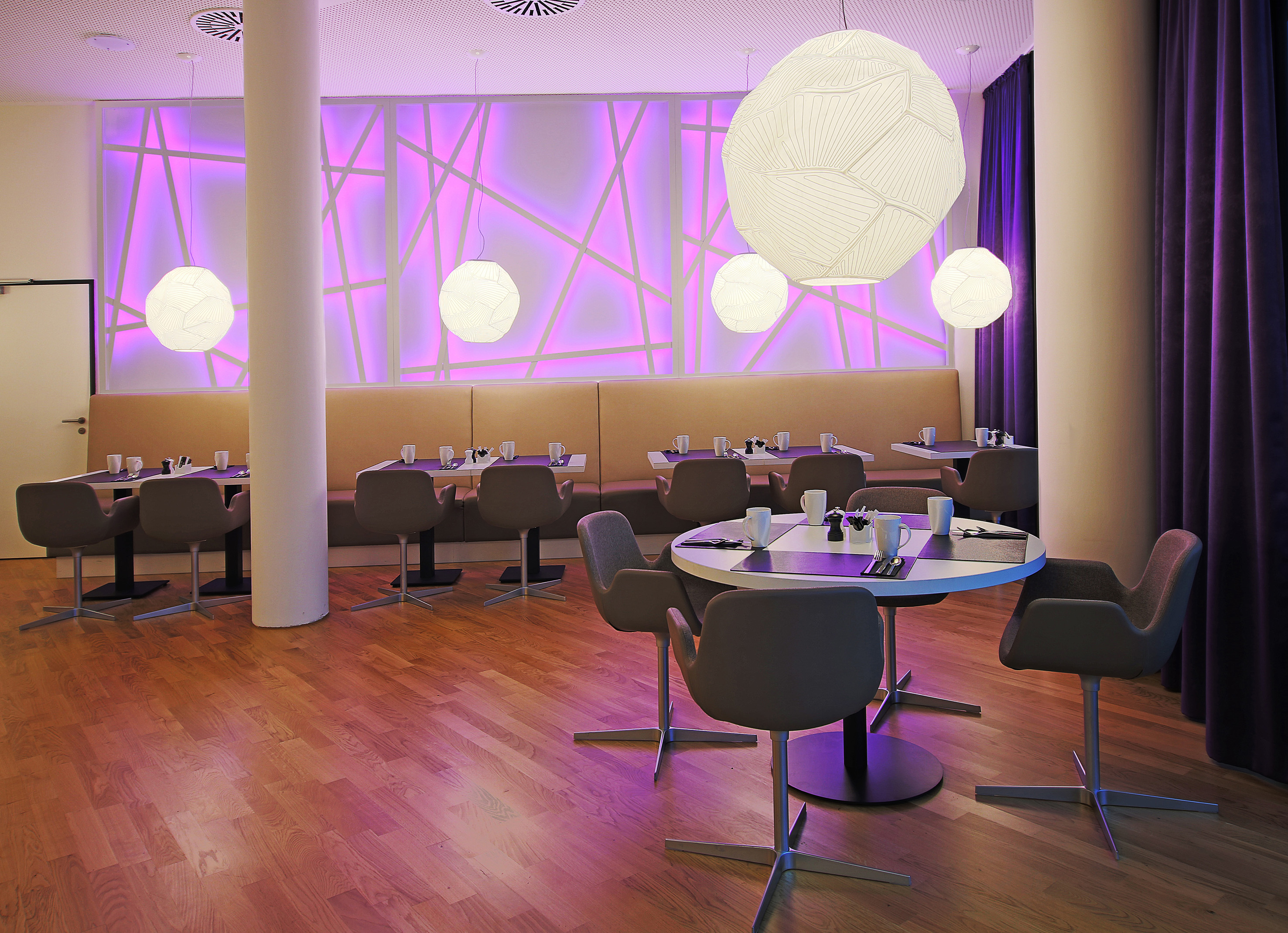 Modern dining area with purple wall lighting, geometric lamps, and set tables.
