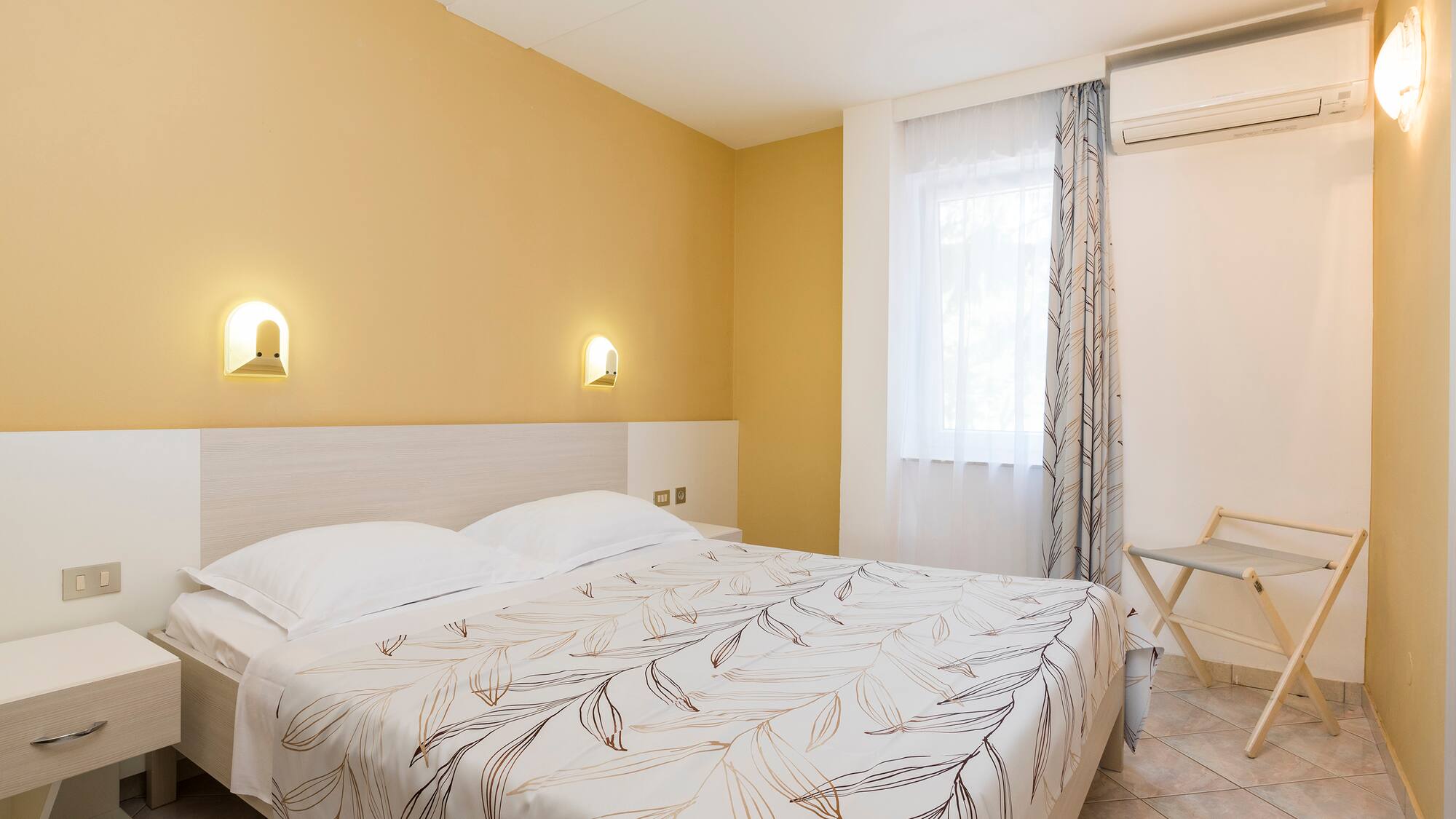 a bed with a white blanket and a chair in a room