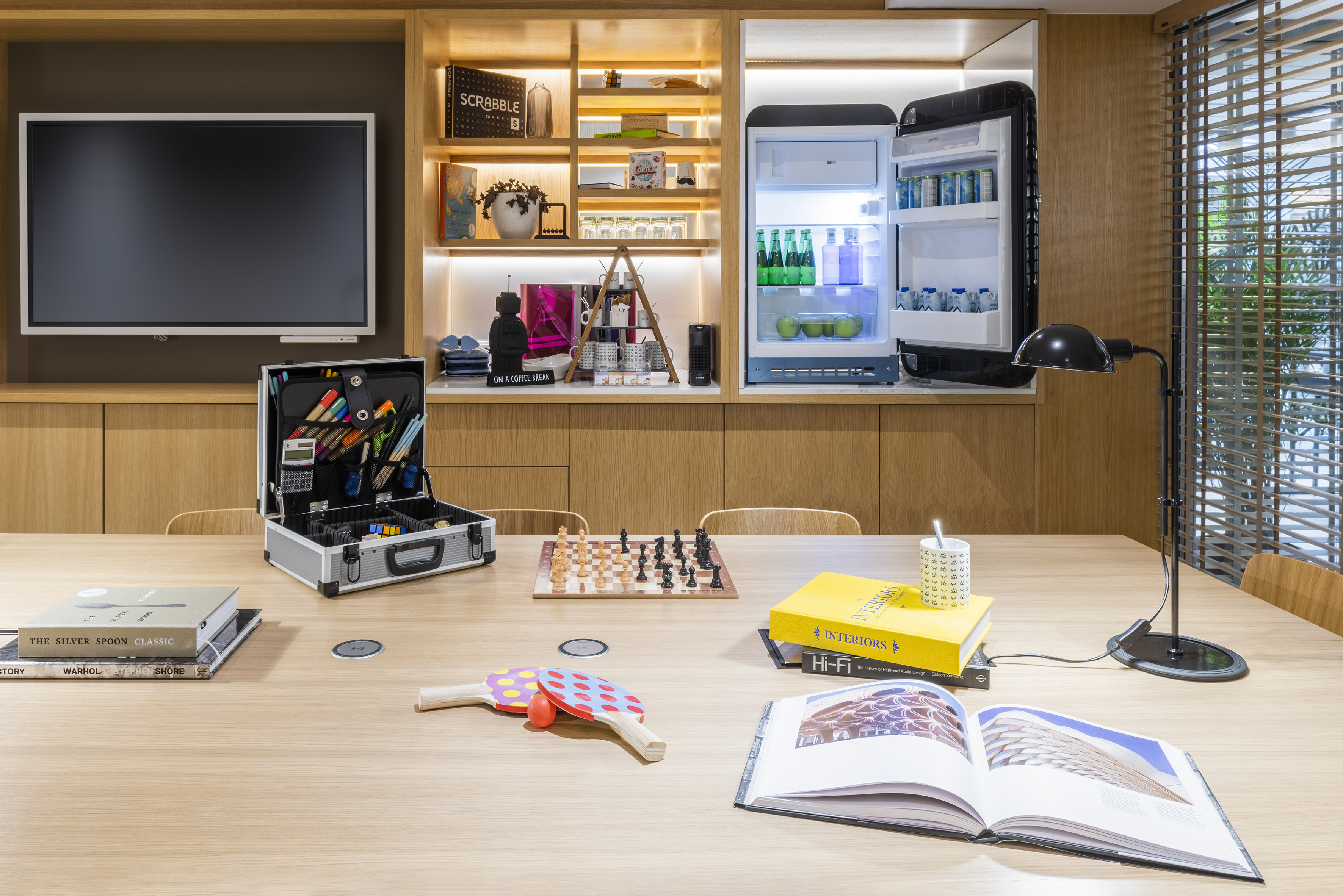 Creative office space with screen, open fridge, art supplies, chess, and books.