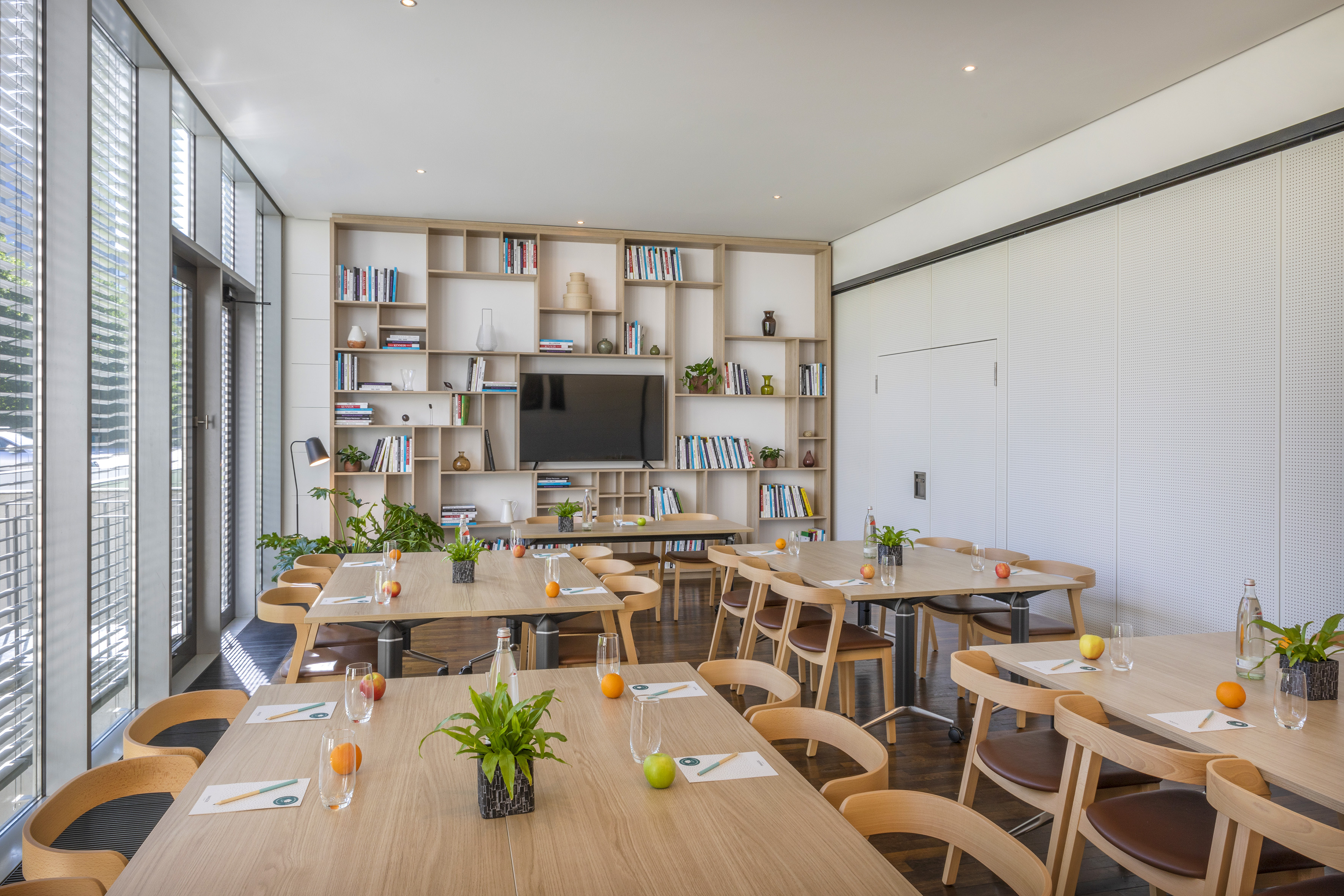 Modern training room with wooden tables, chairs, windows, and a bookshelf. - Meeting Box - INNSiDE Düsseldorf Seestern, Düsseldorf