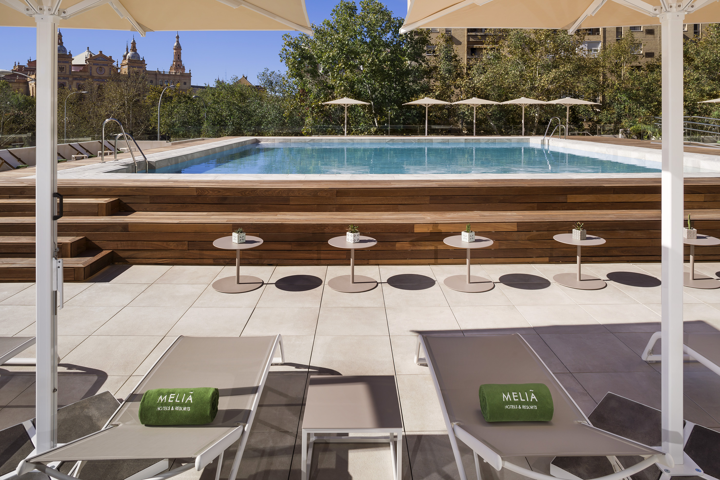 Meliá hotel rooftop pool, wooden deck, sun loungers, umbrellas, city view.