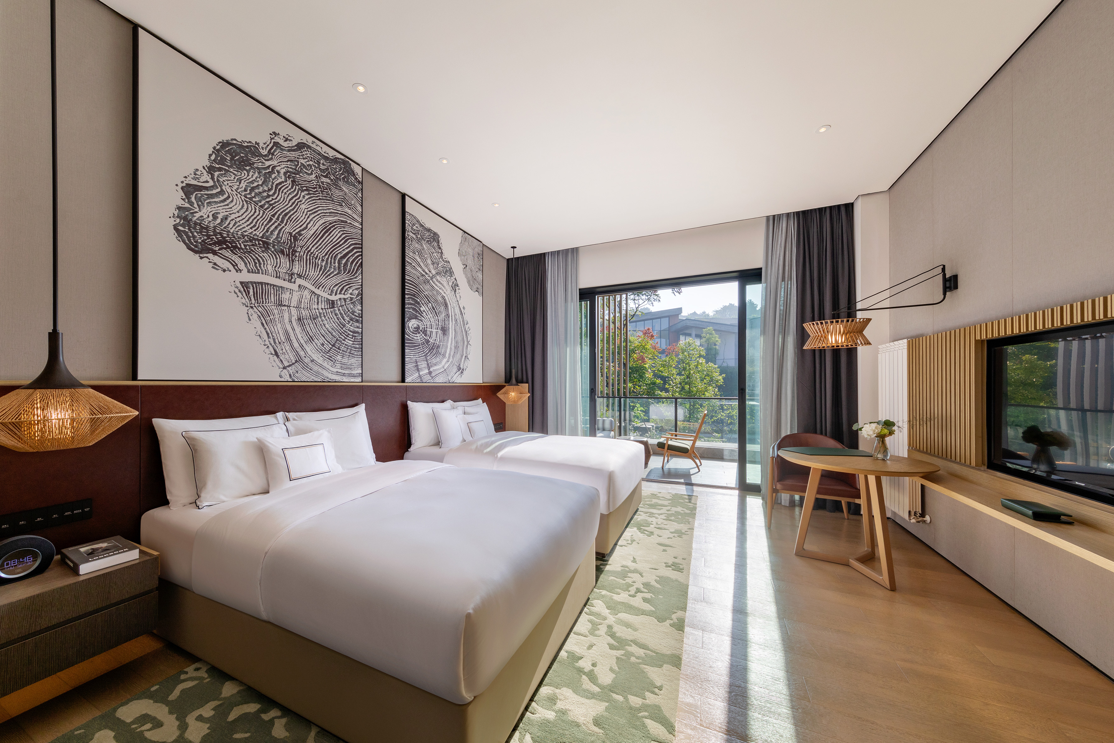 Modern hotel room with two beds, balcony, nature view, and tree ring art.