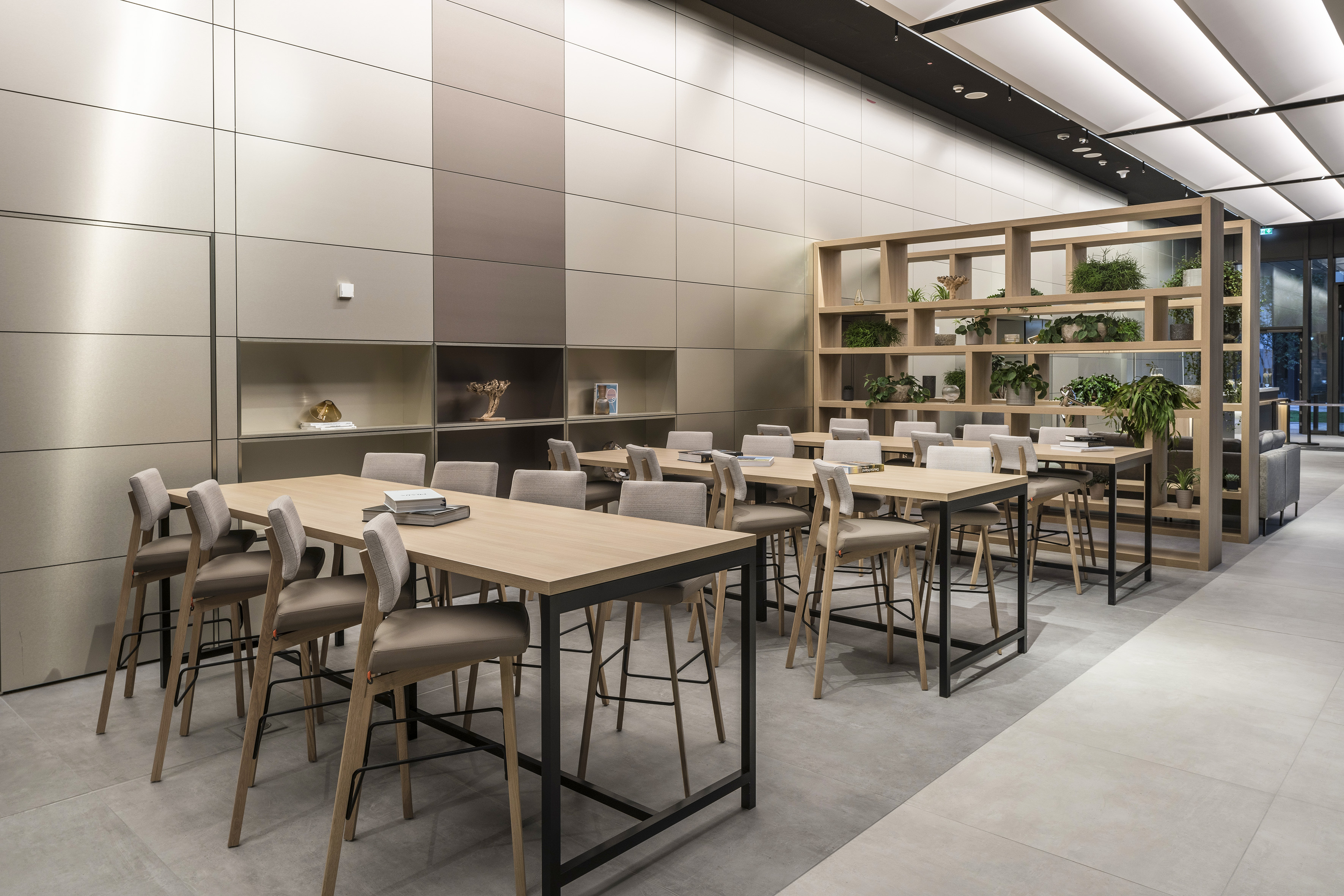 Modern office collaboration space with high tables, bar stools, and plants.