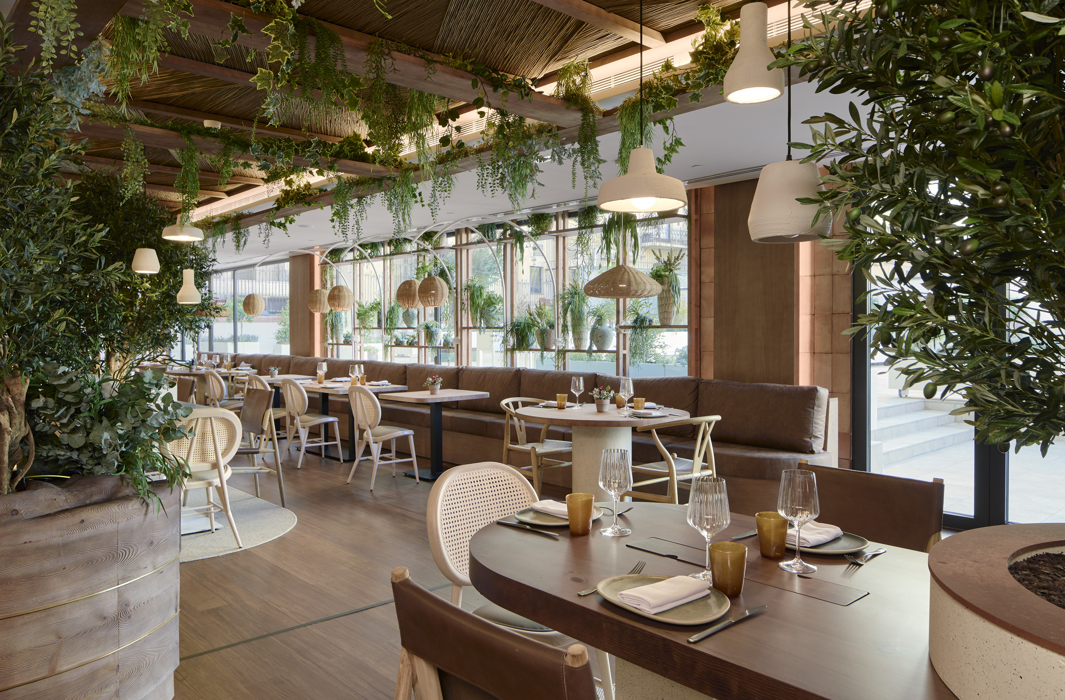 Modern restaurant interior with lush greenery, natural wood tables, and rattan chairs.