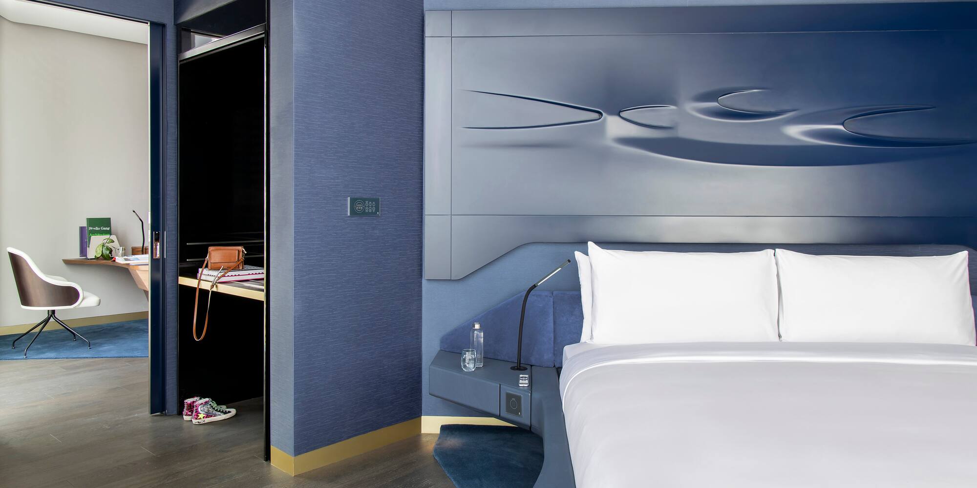 Luxury blue hotel bedroom with sculptural headboard and adjacent work desk.
