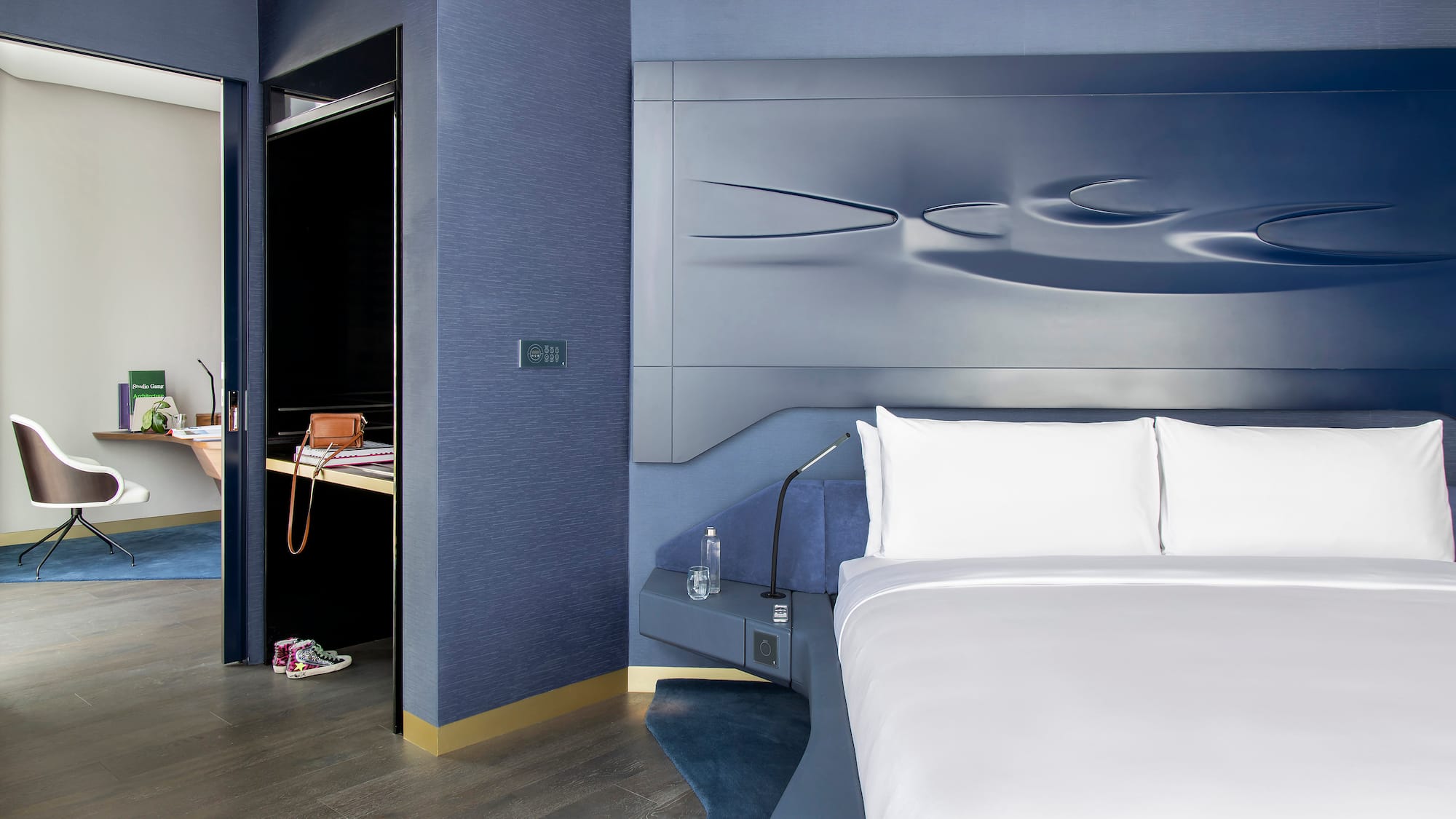 Luxury blue hotel bedroom with sculptural headboard and adjacent work desk.