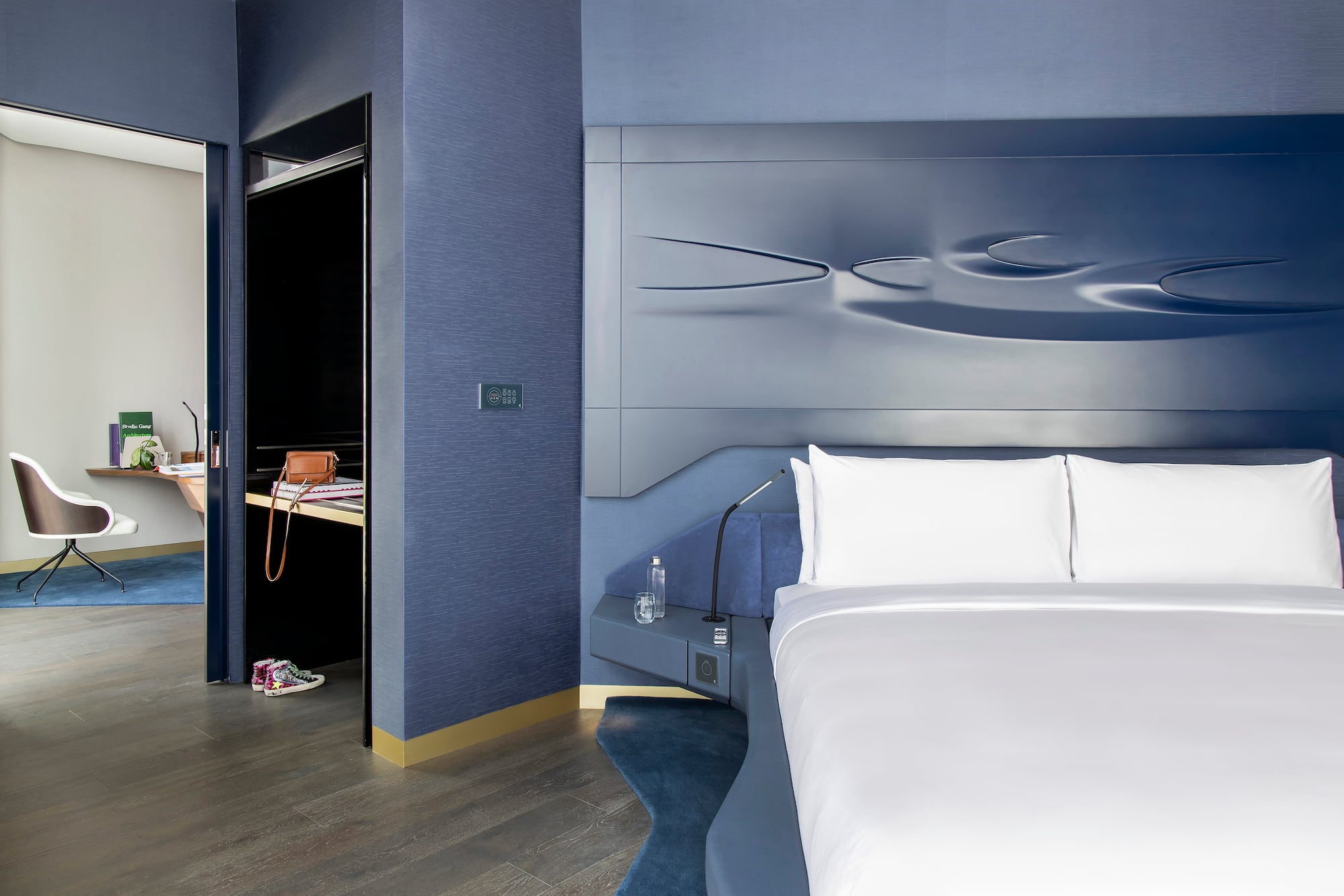 Luxury blue hotel bedroom with sculptural headboard and adjacent work desk.