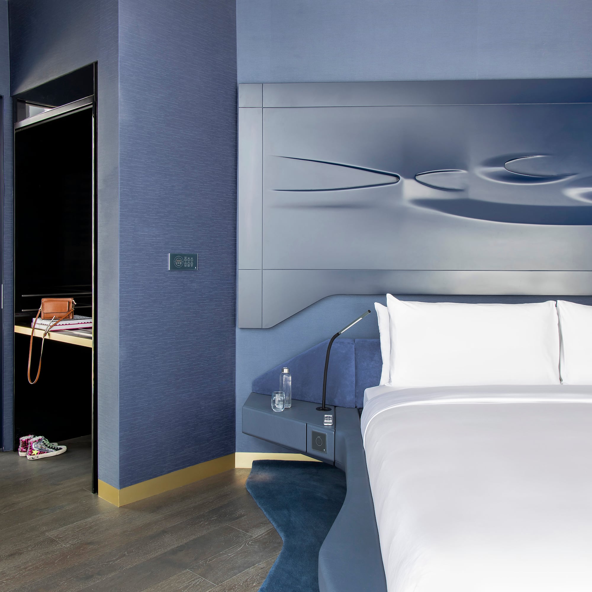 Luxury blue hotel bedroom with sculptural headboard and adjacent work desk.