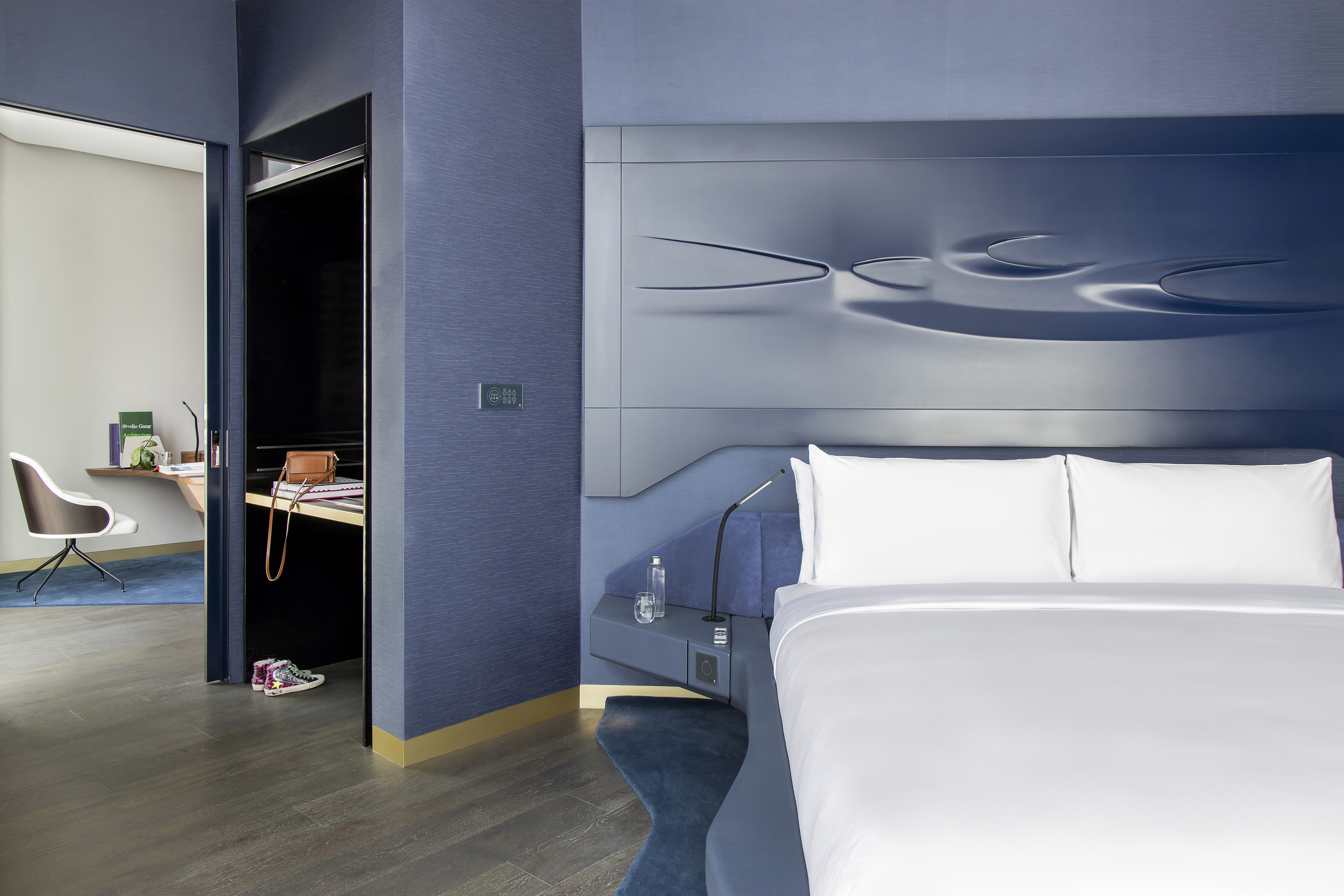 Luxury blue hotel bedroom with sculptural headboard and adjacent work desk.