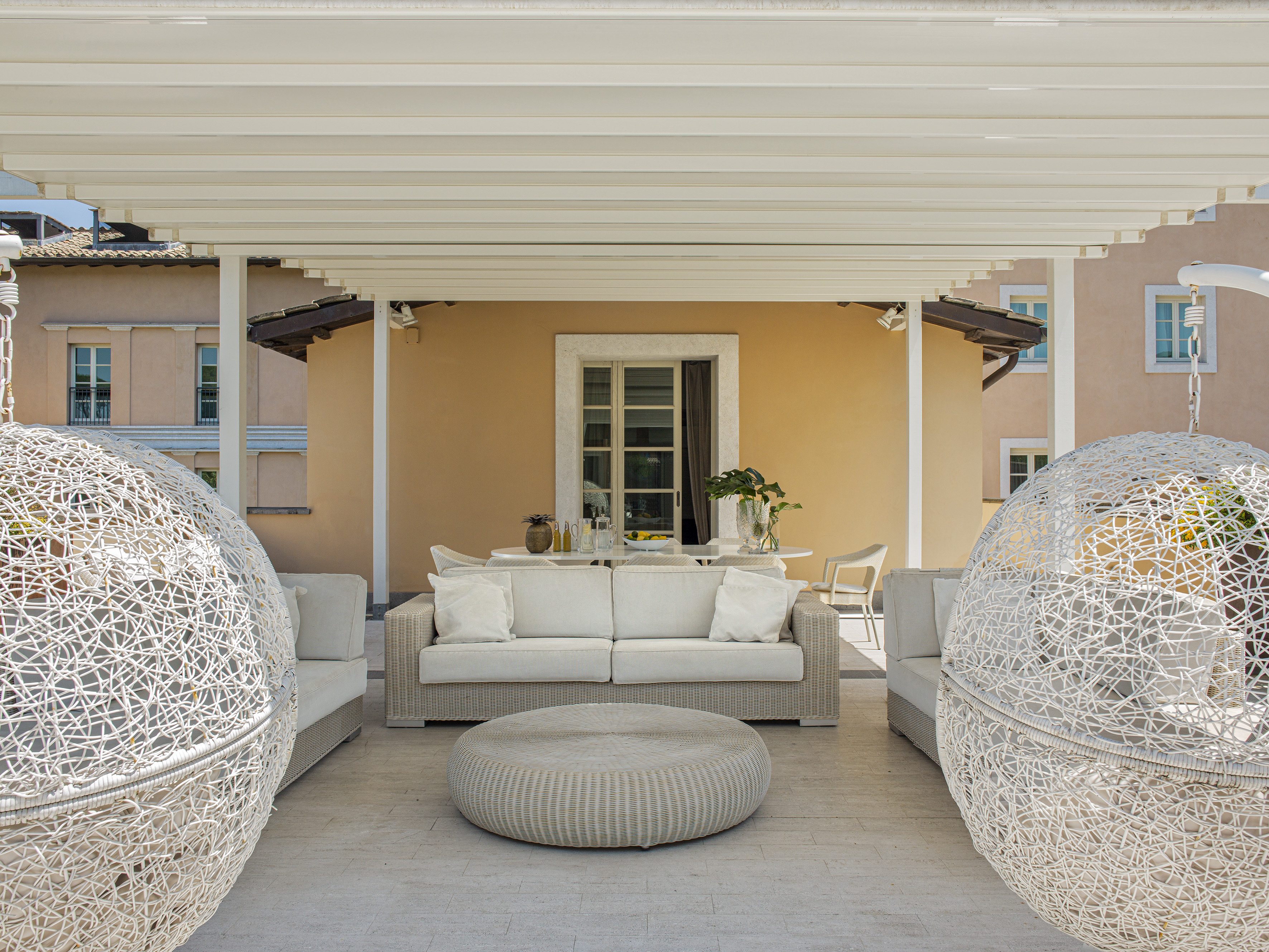 Outdoor patio with pergola, modern wicker sofa, ottoman, and spherical lounge chairs.