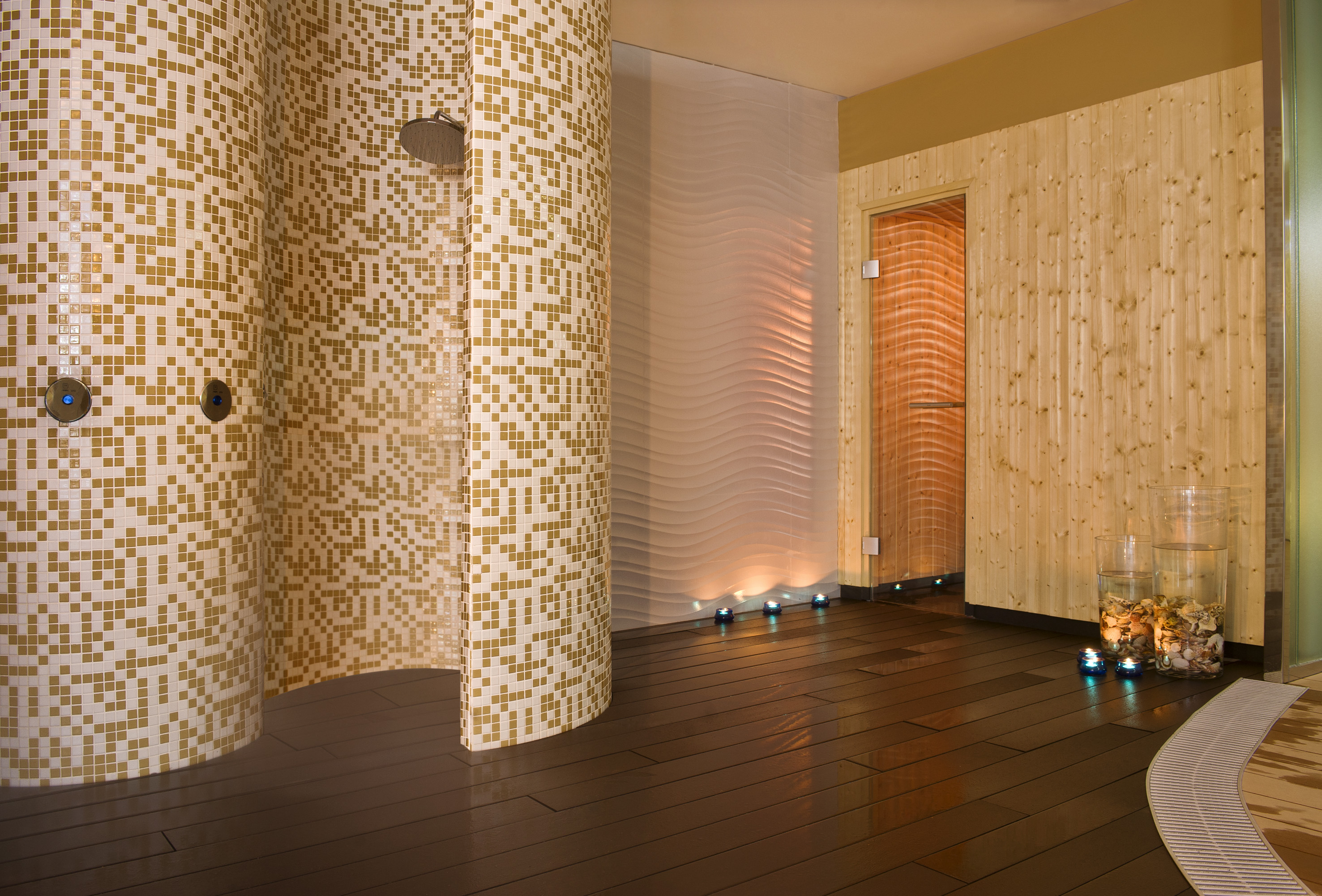 Gold mosaic shower, wooden sauna room, and wavy wall in a modern spa.