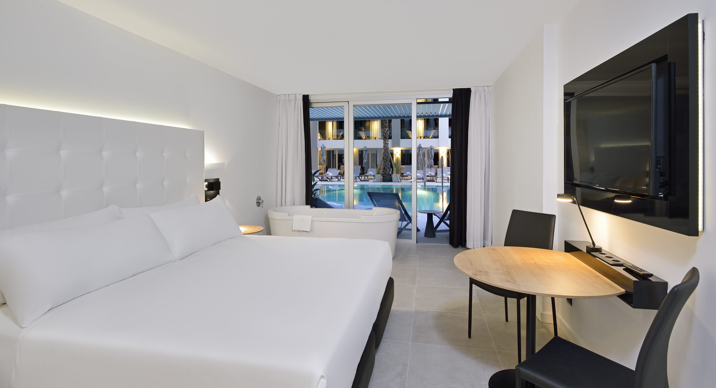 Contemporary suite with white bed, freestanding tub, and pool patio access.