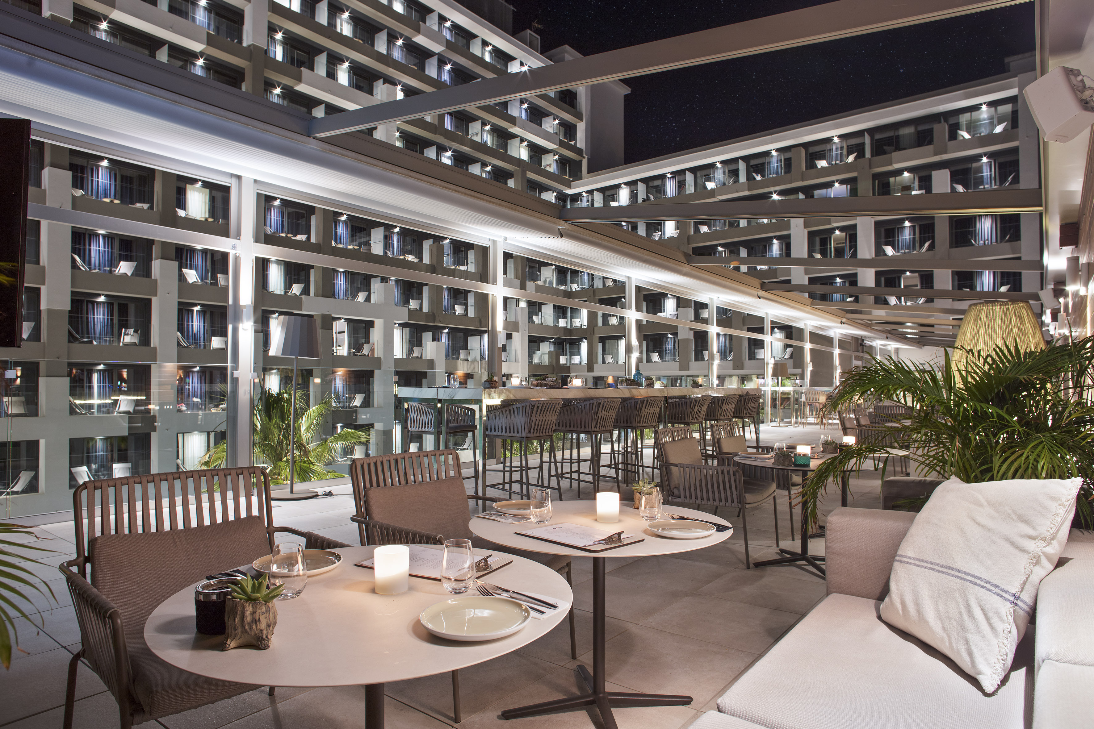 Modern outdoor bar and restaurant terrace at night with illuminated hotel.