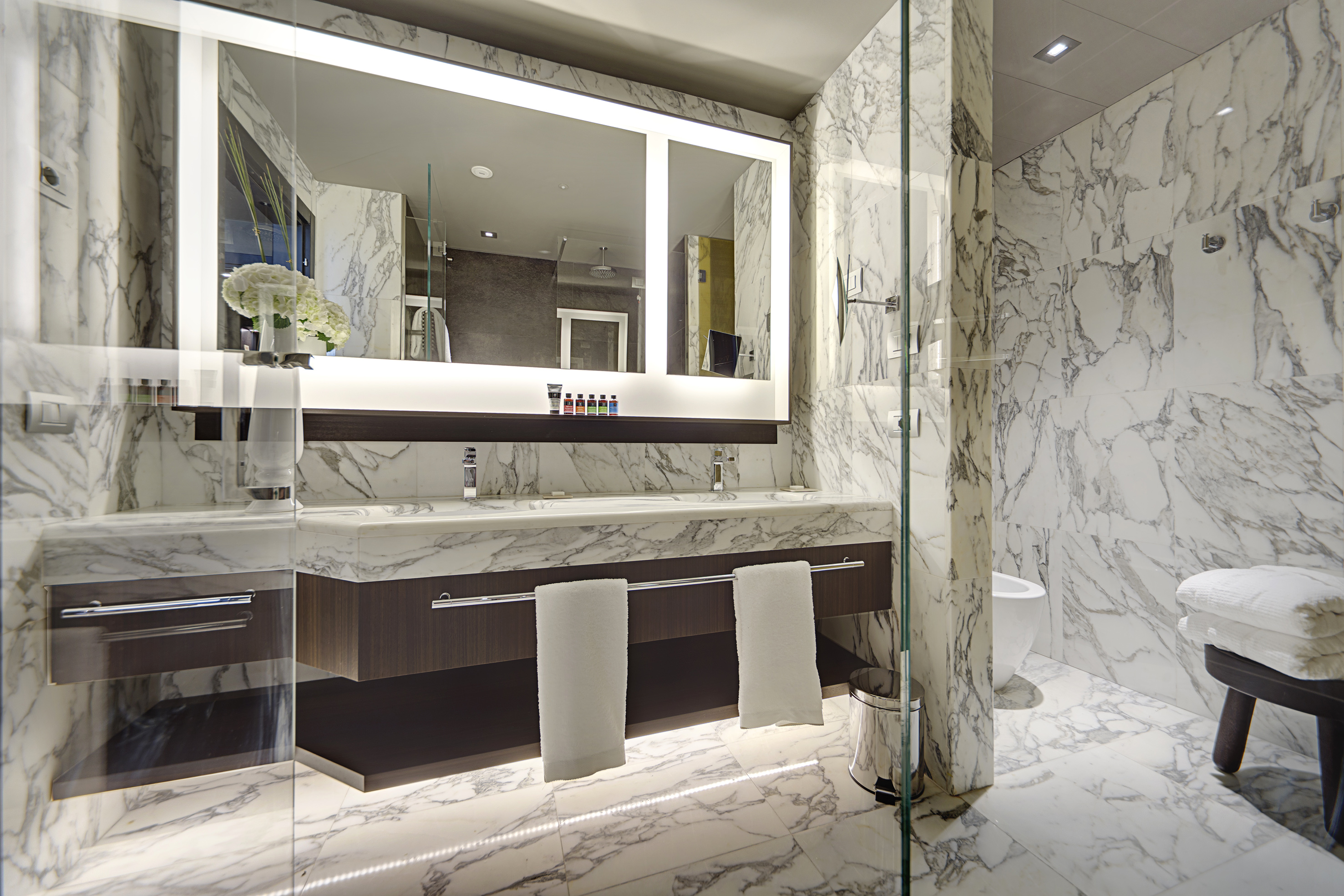 Luxury marble bathroom with double vanity, illuminated mirror, and glass shower.