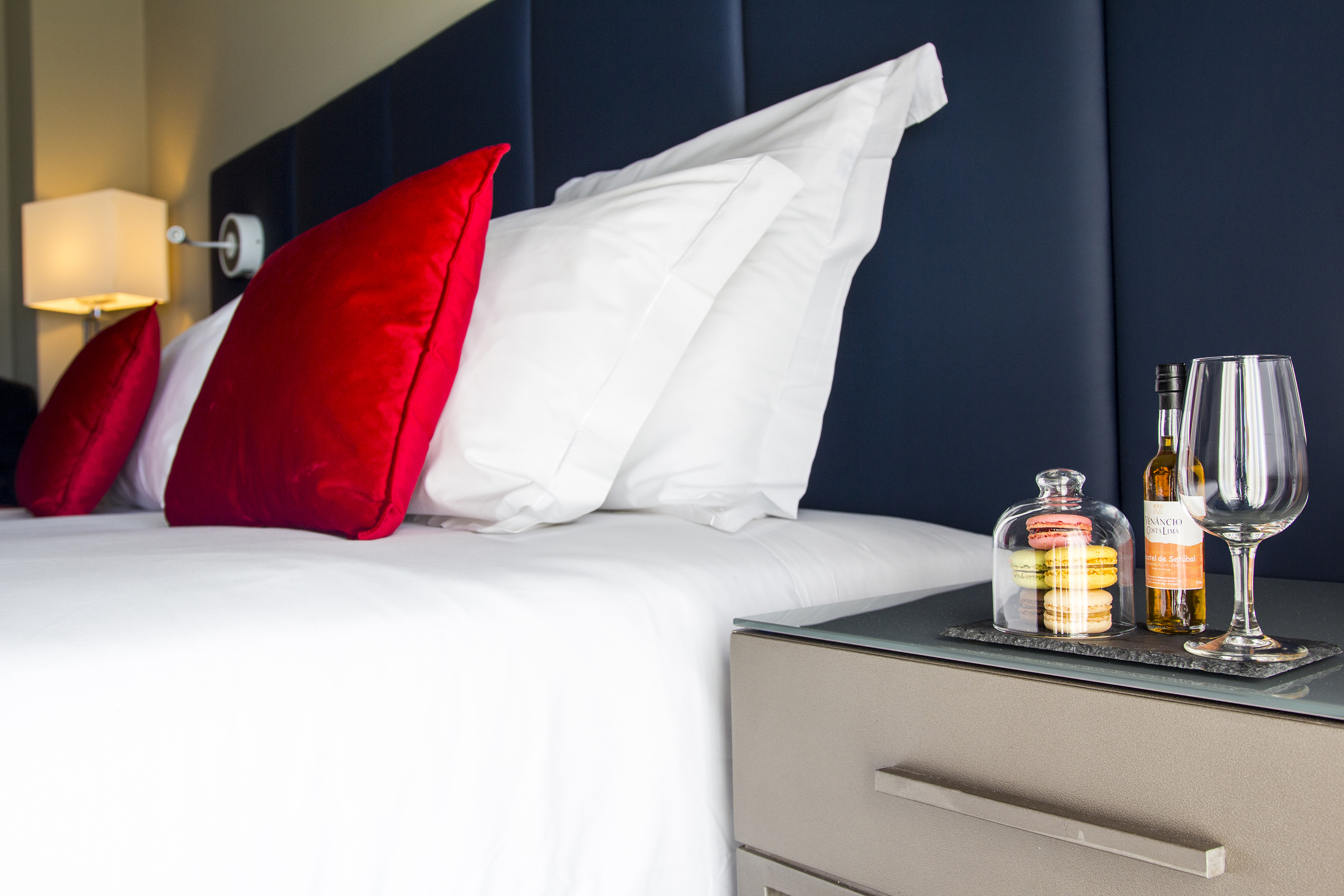 Luxury hotel bed with red pillows, macarons, wine bottle, and glass on nightstand.