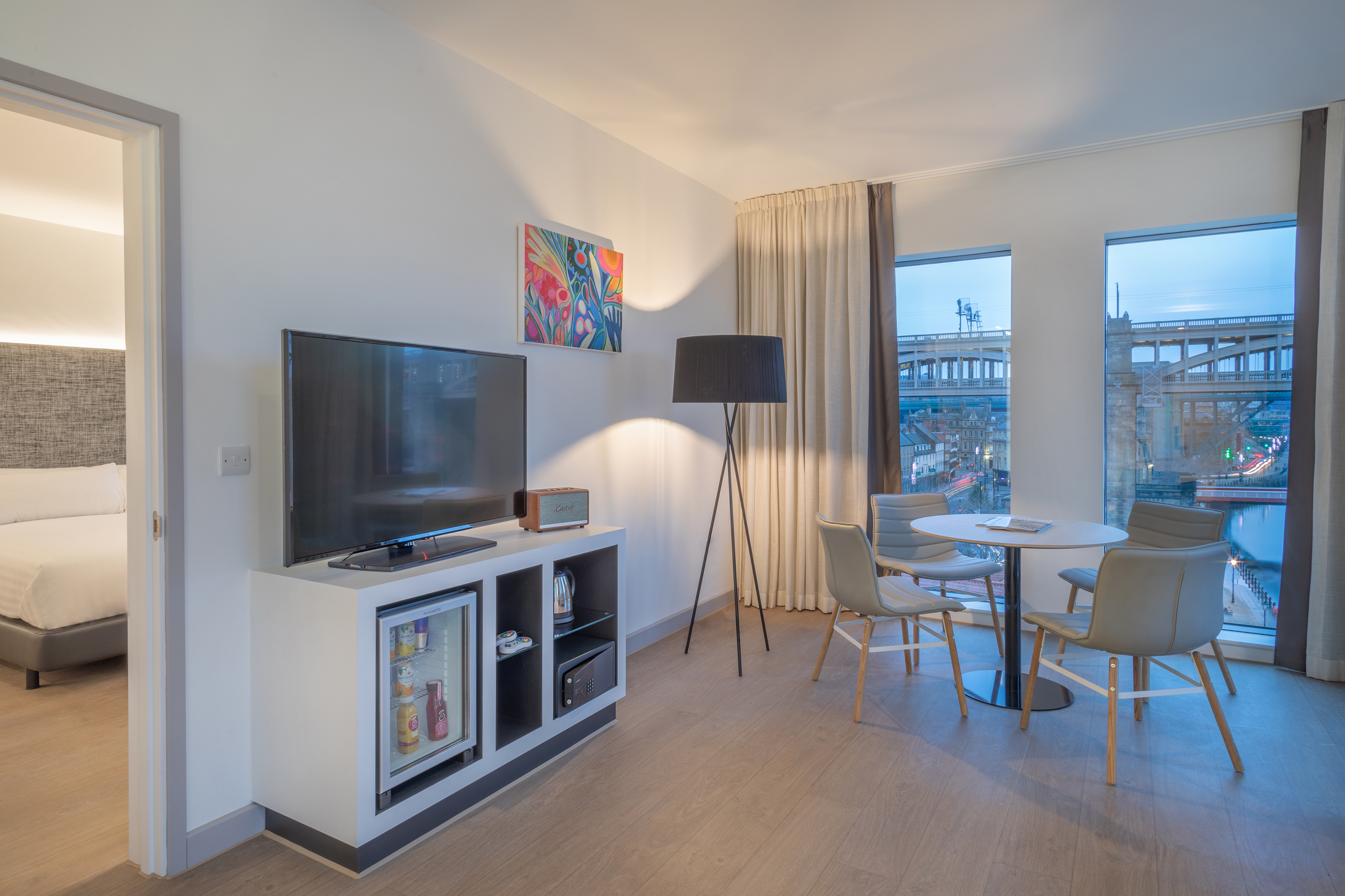 Modern hotel suite with living area, TV, dining, and city bridge view.