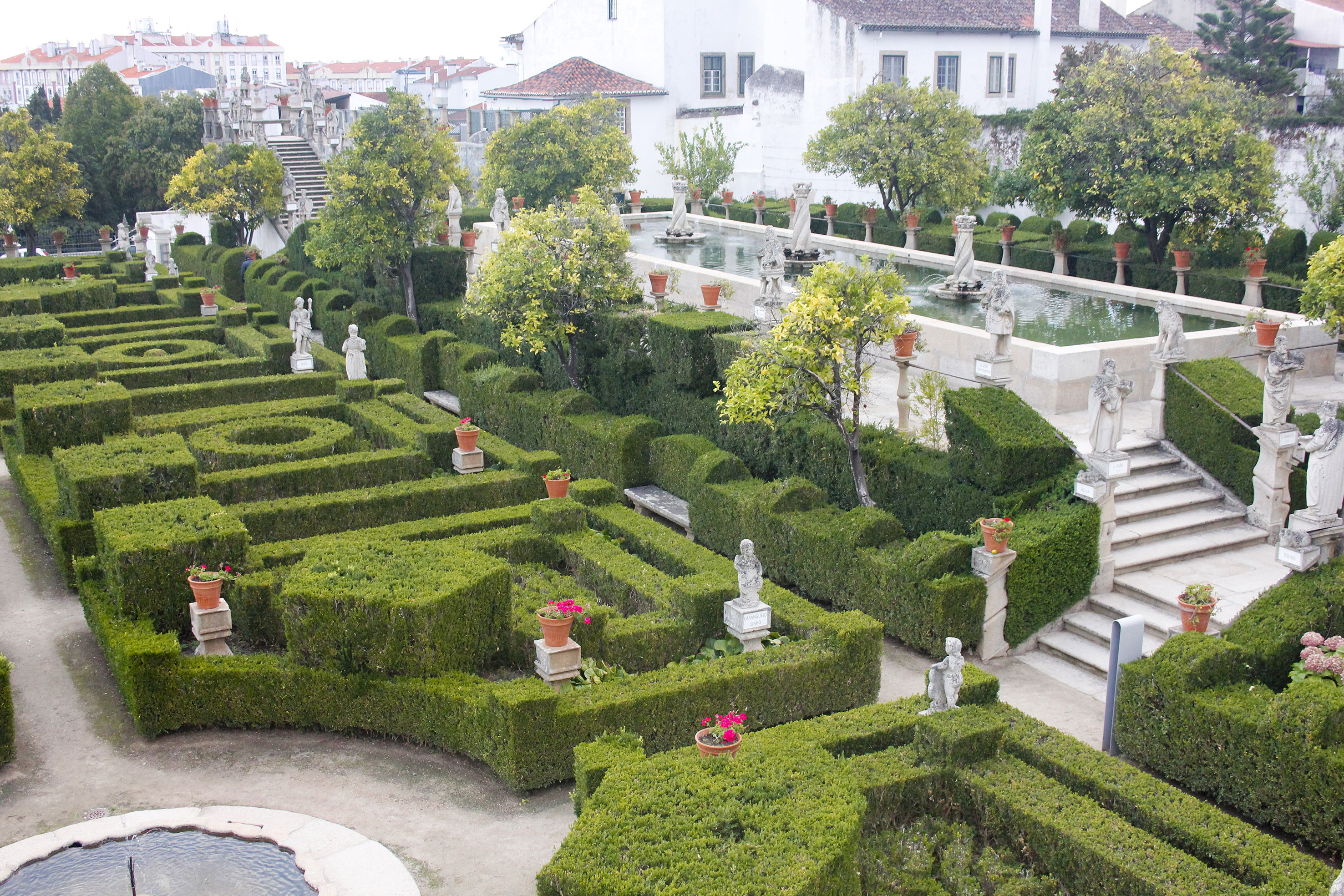 Formal garden with geometric hedges, classical statues, and decorative fountain.