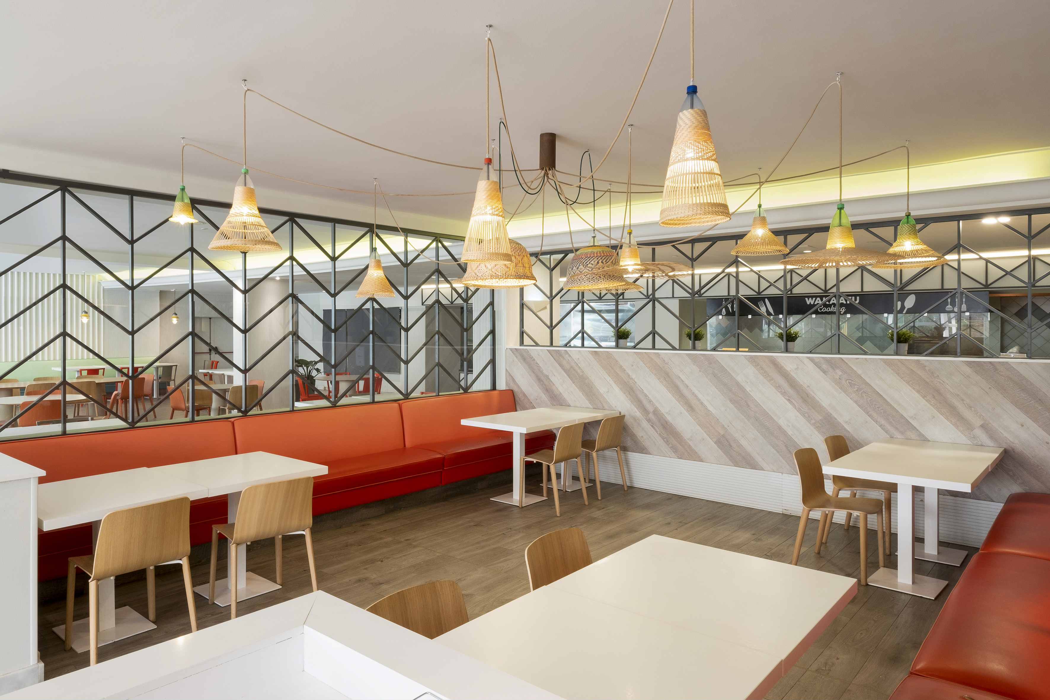 Bright restaurant interior with orange seating, white tables, and woven pendant lamps.