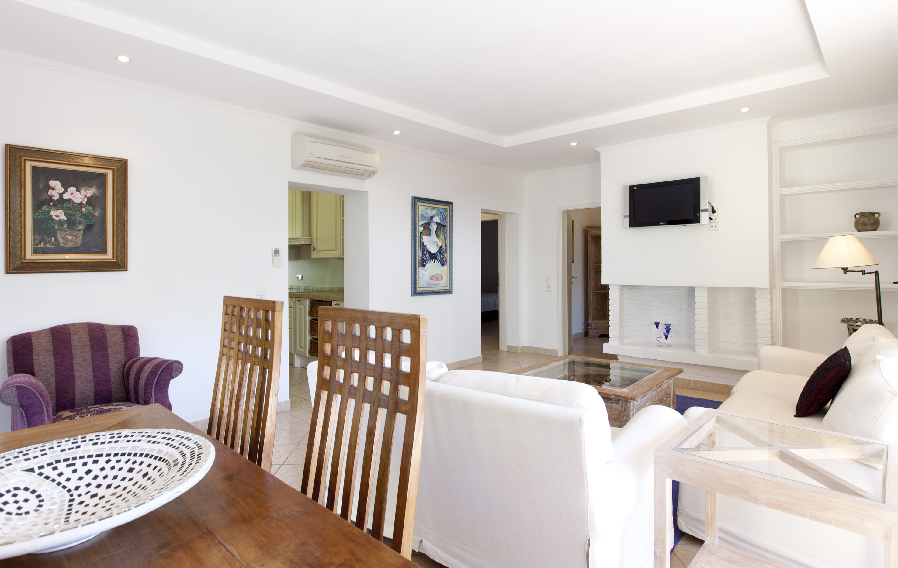 White living dining room interior with wooden table, comfy sofas, fireplace.