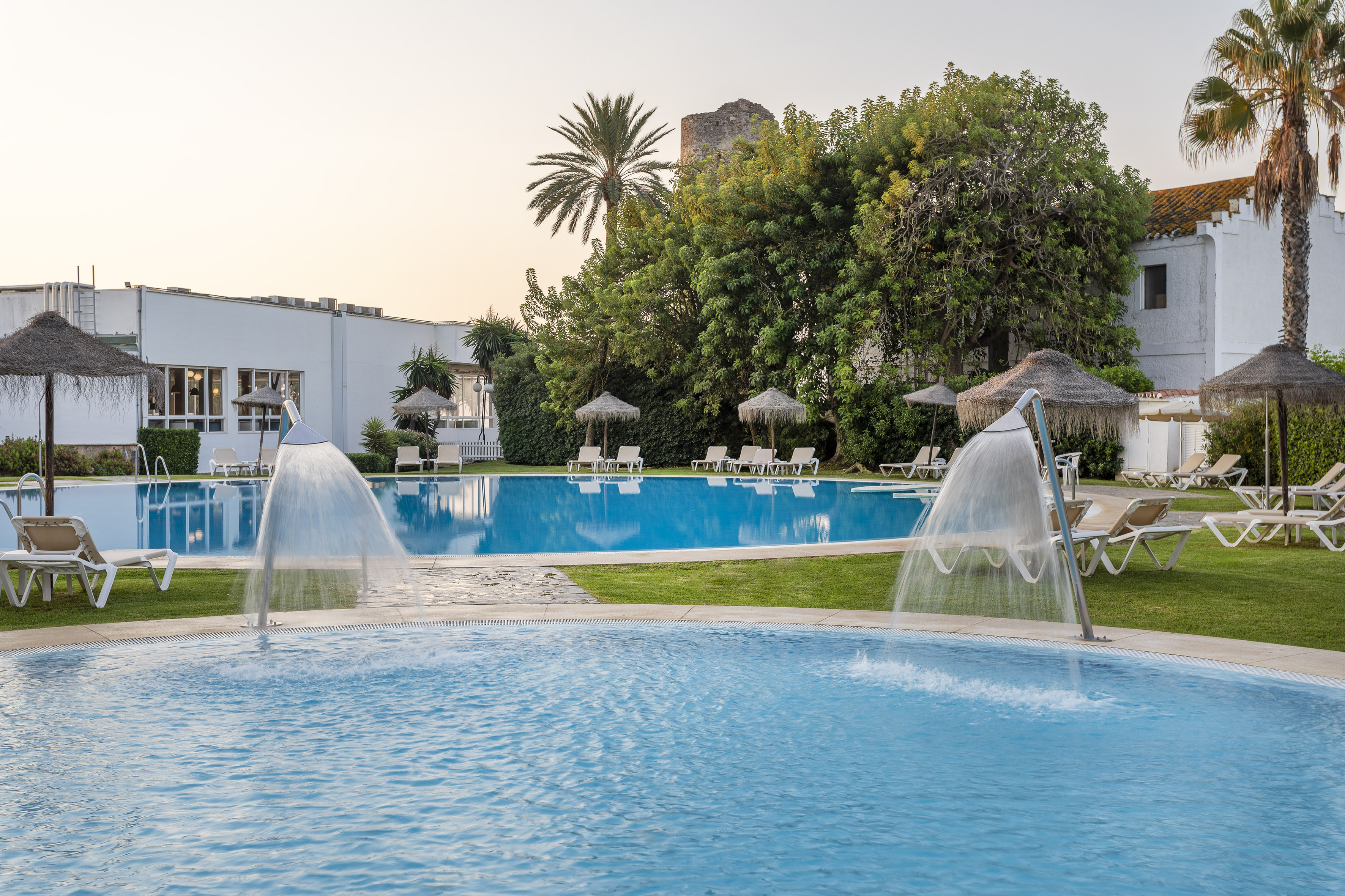 Resort swimming pools with fountains, sun loungers, and palm trees.