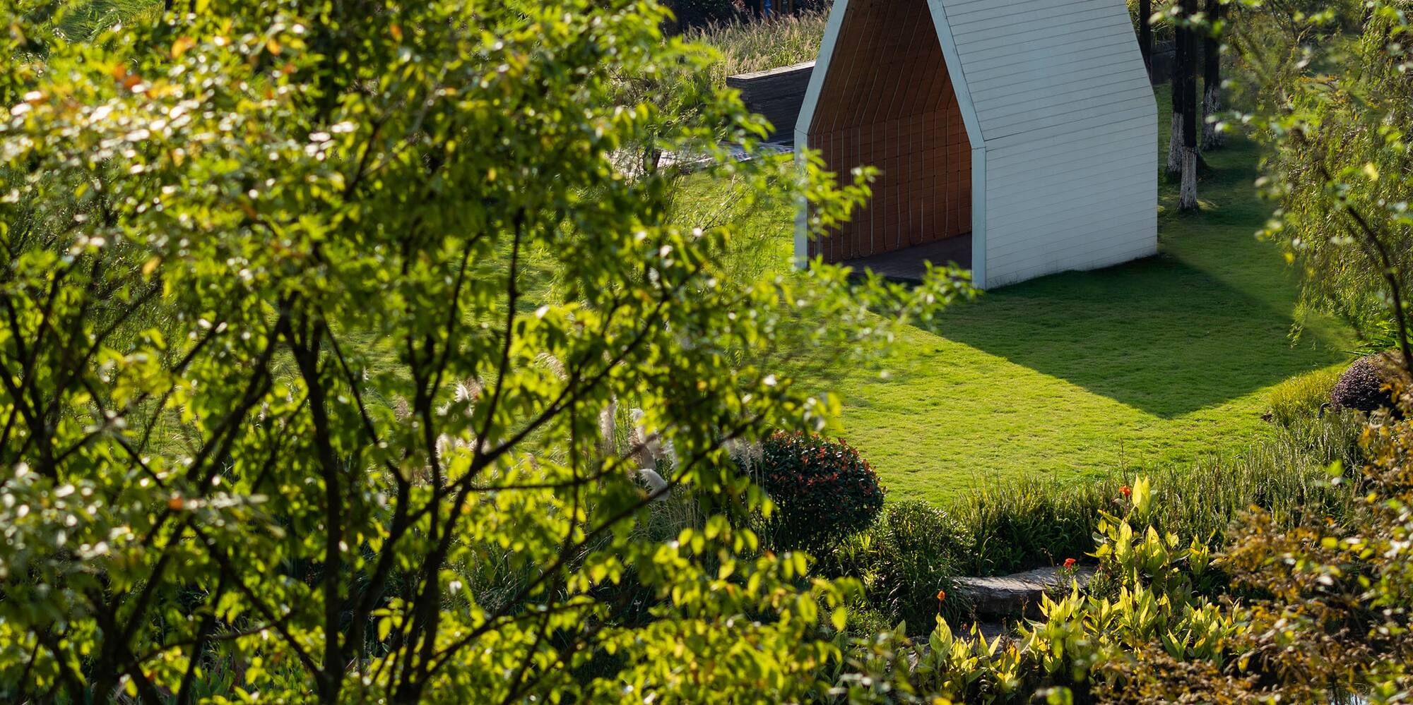 a small white structure in a grassy area with trees and a pond