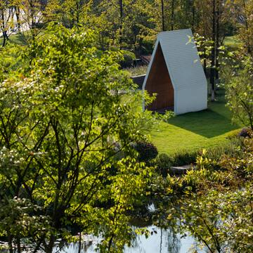 a small white structure in a grassy area with trees and a pond