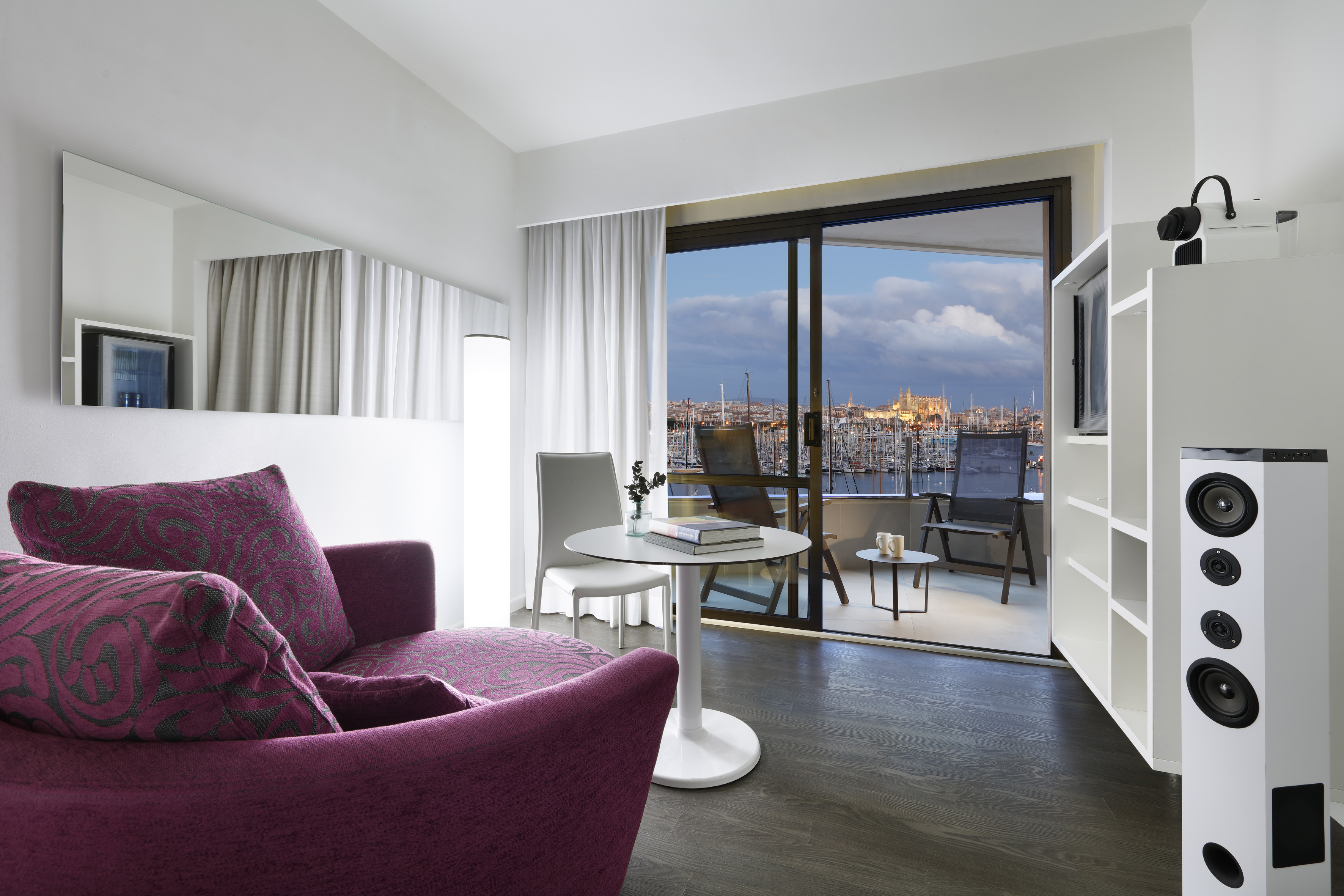 Modern hotel suite with purple armchair, balcony, and scenic marina city view.
