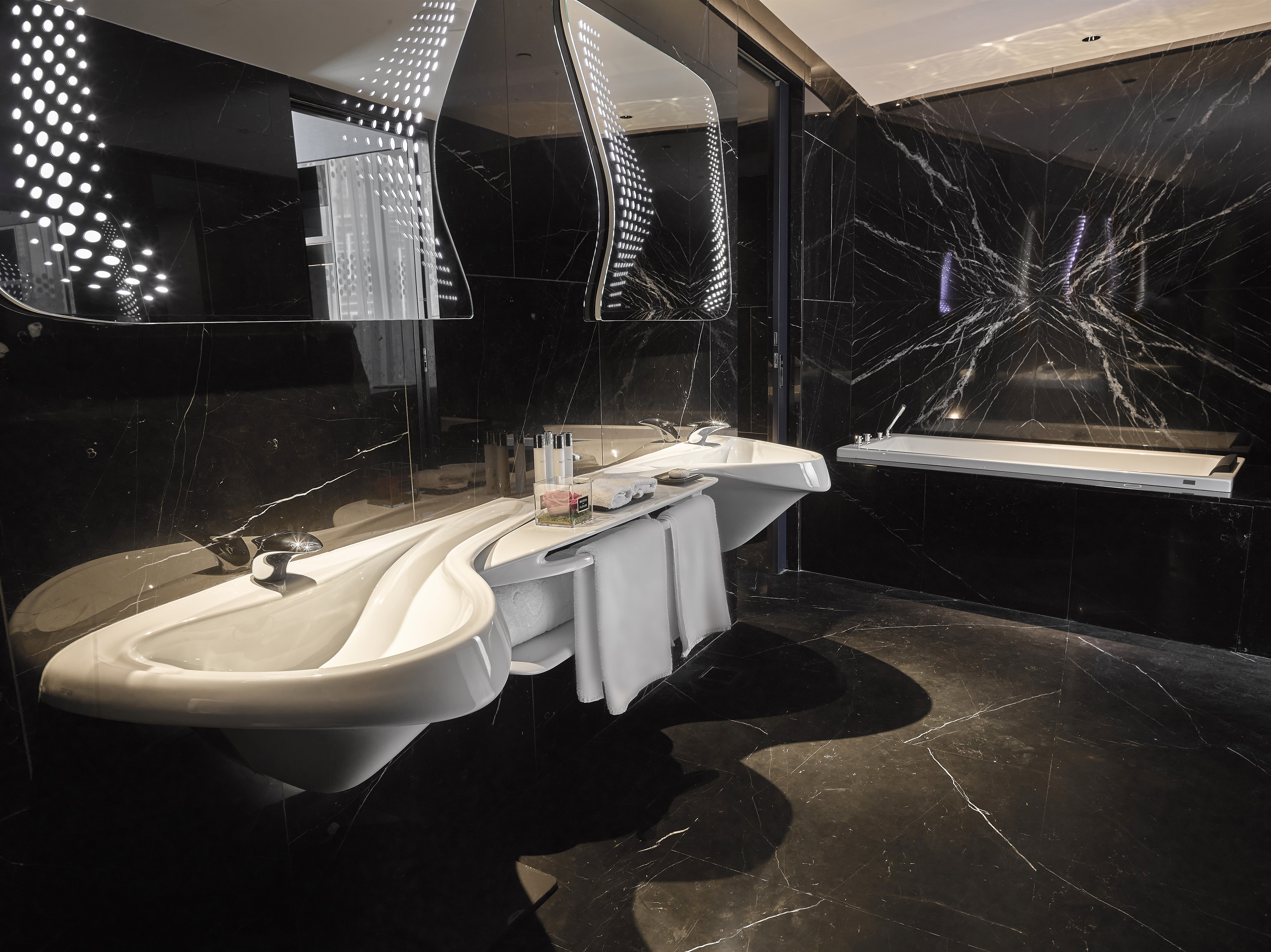 Modern black marble bathroom, sculptural double vanity, illuminated mirrors.