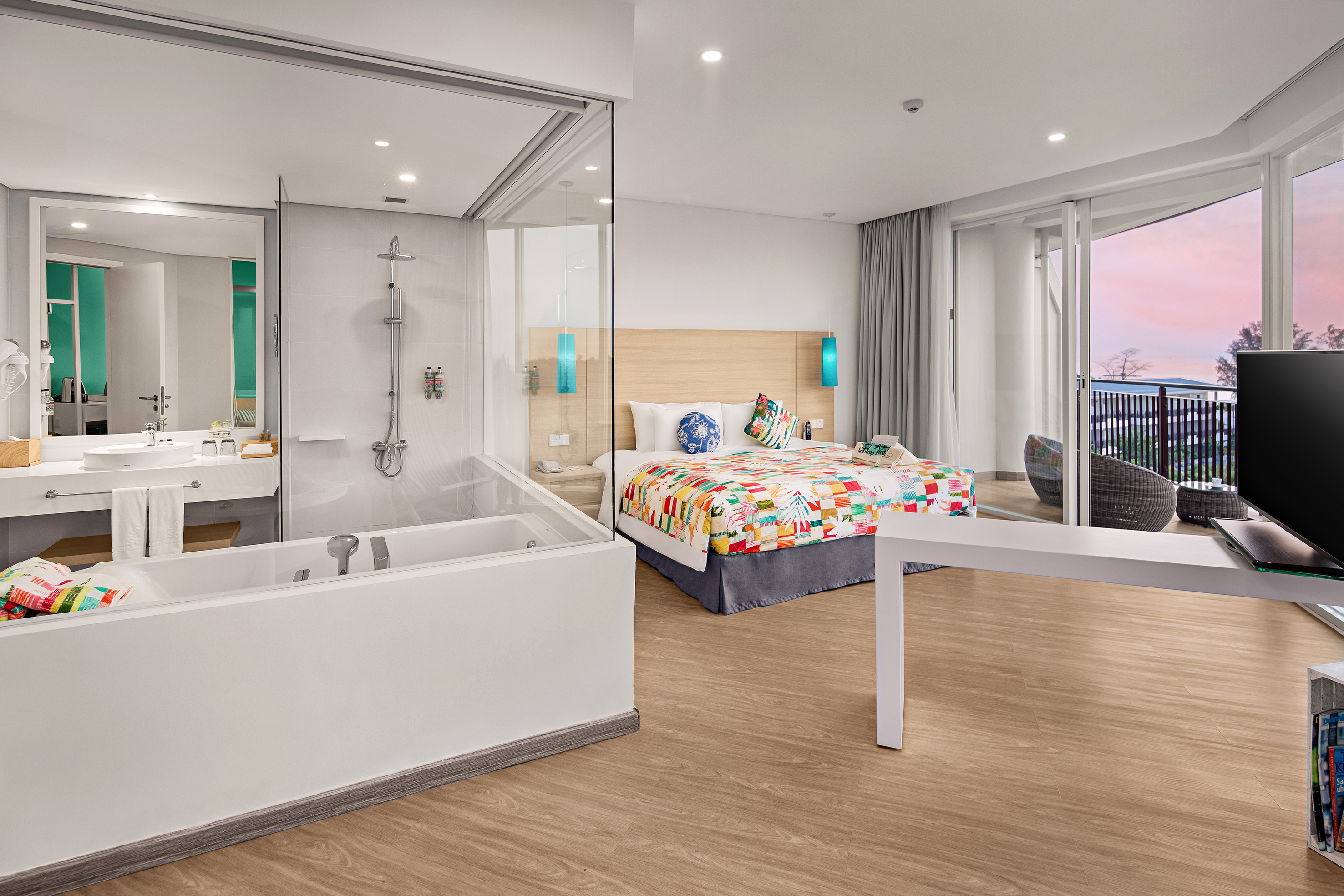 Modern hotel room: colorful bed, open bathroom, bathtub, and balcony.