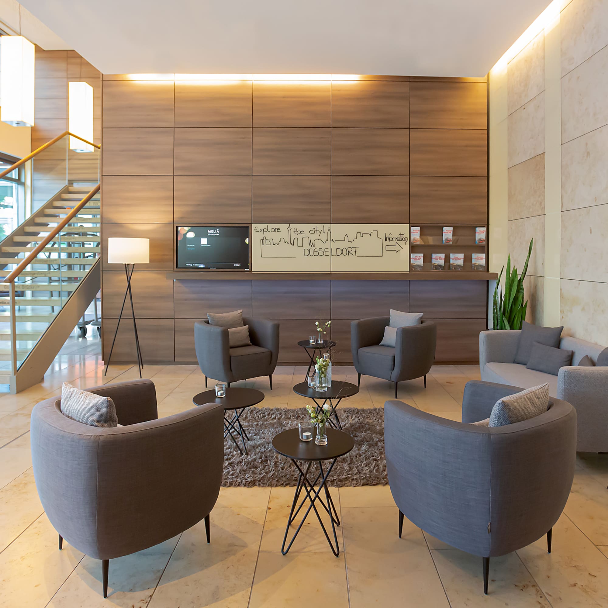Modern hotel lobby in Dusseldorf with gray lounge seating and a grand staircase.