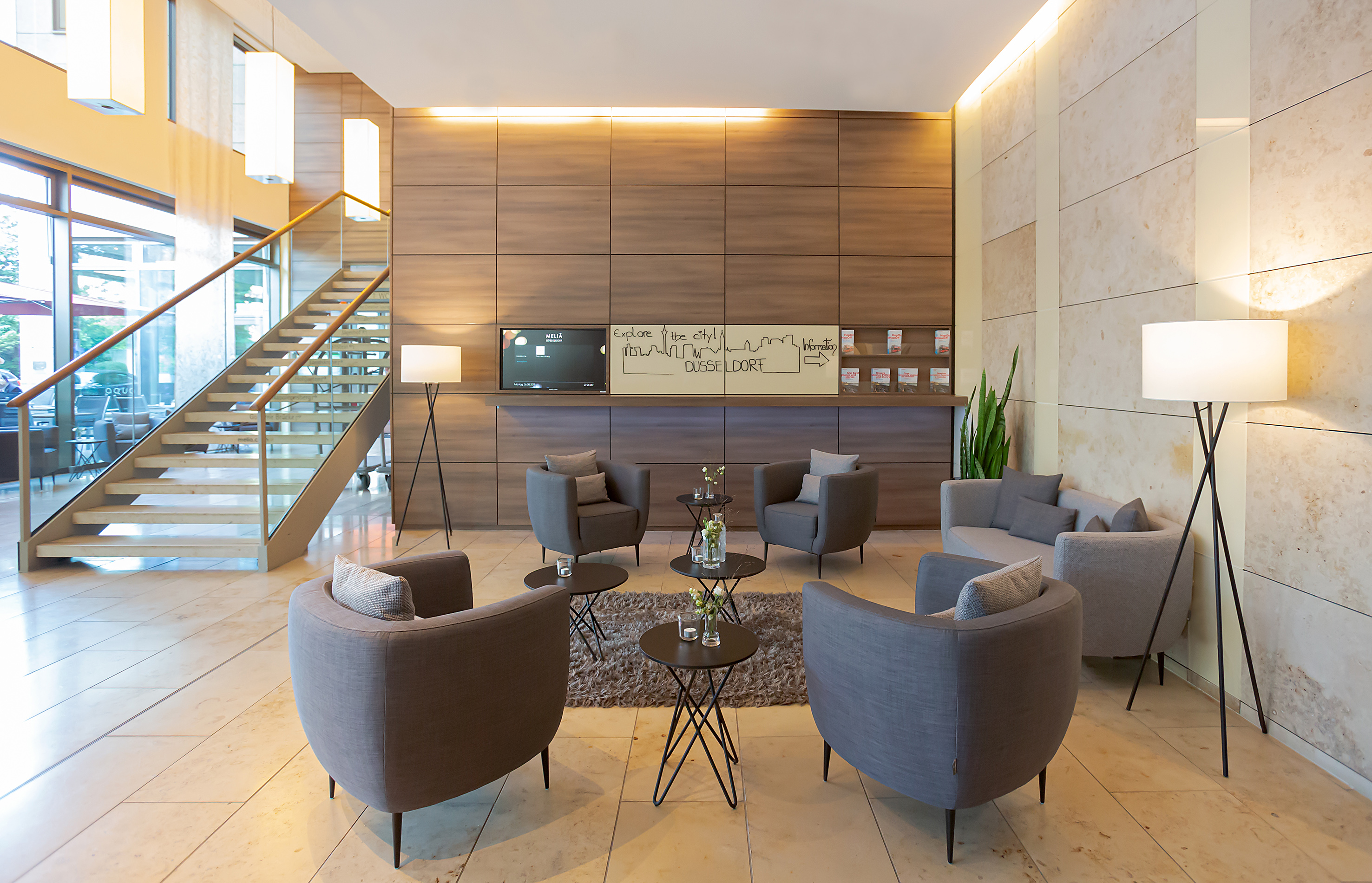 Modern hotel lobby in Dusseldorf with gray lounge seating and a grand staircase.