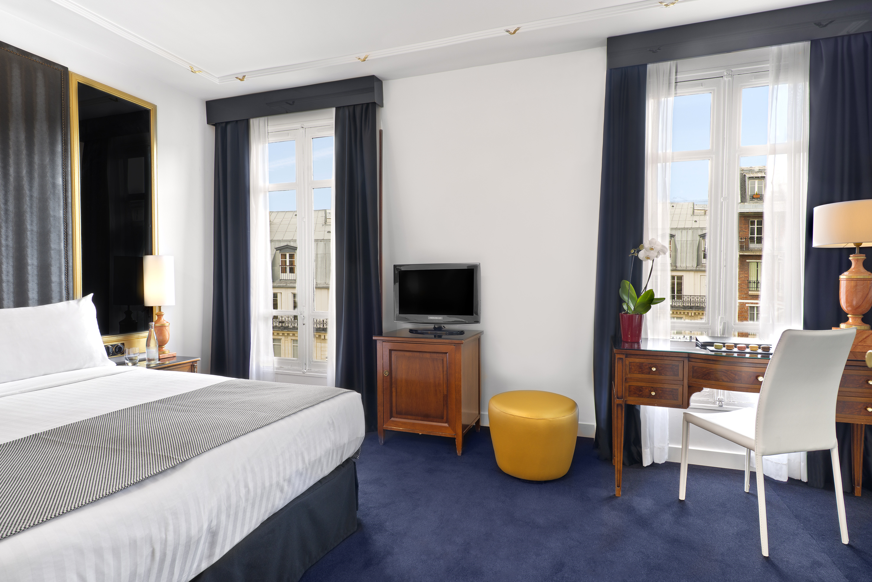 Luxurious Parisian hotel bedroom with bed, desk, and city view from window.