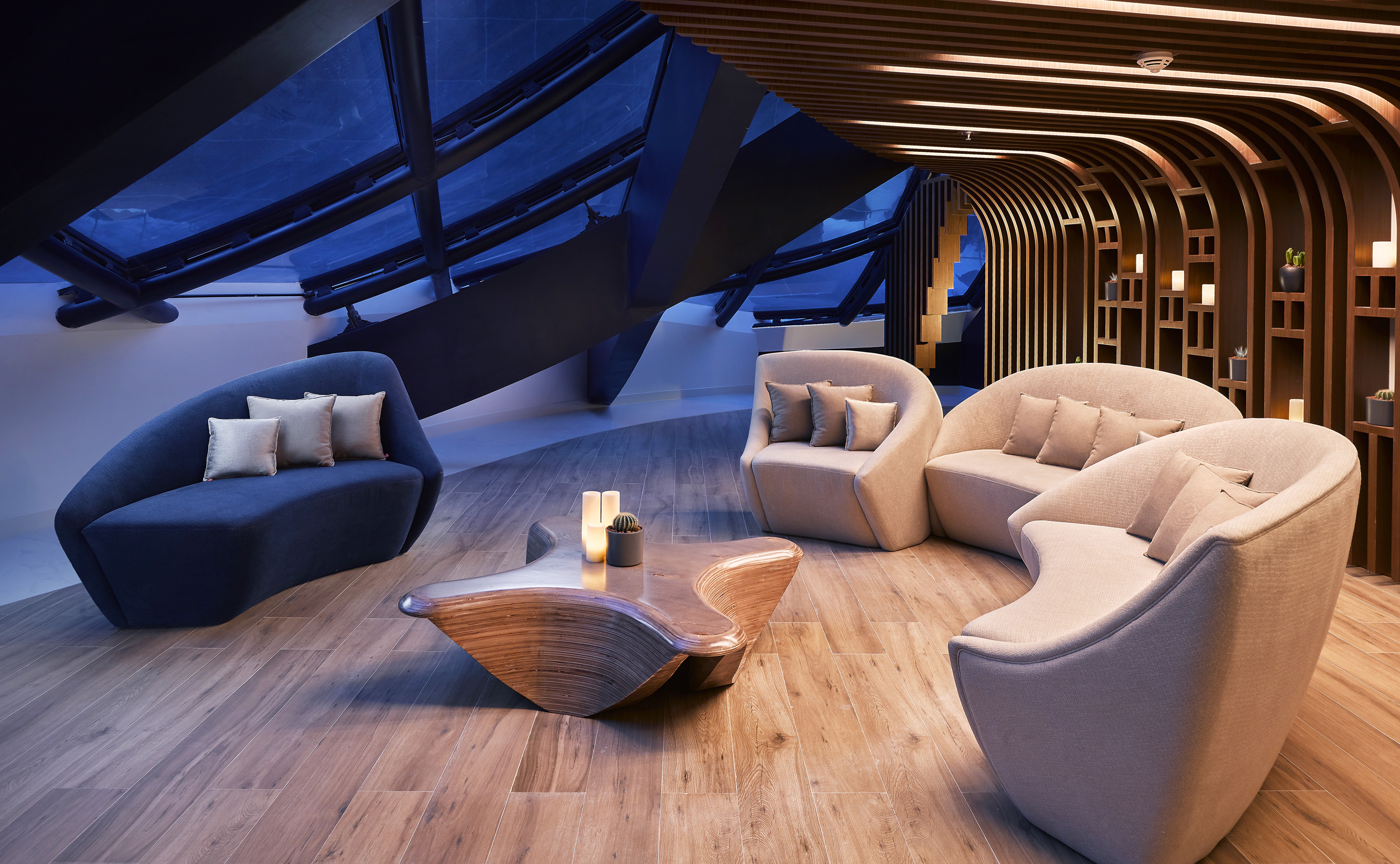 Modern hotel lounge, curved sofas, wooden ceiling, coffee table, and ambient lighting.