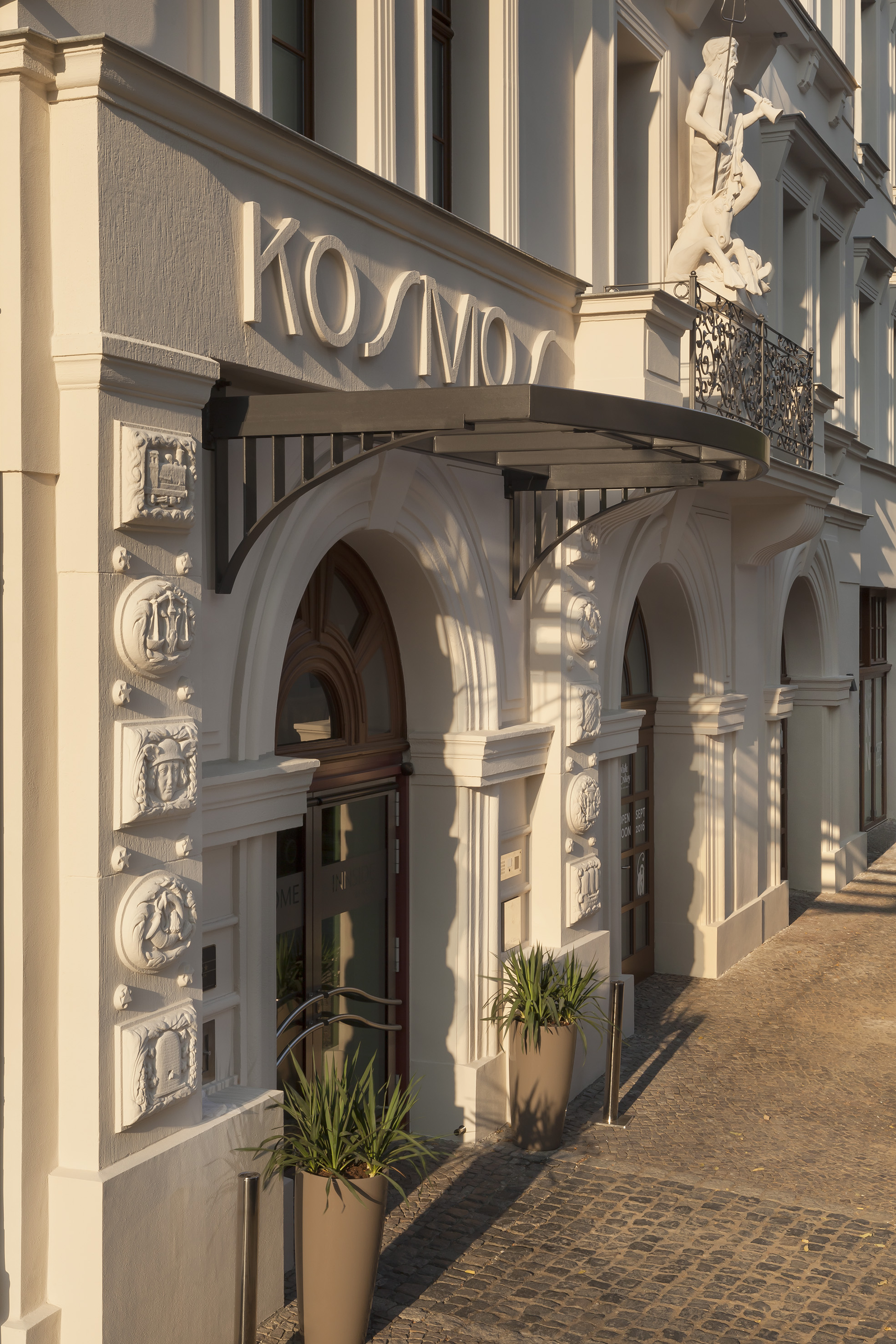 Kosmo hotel facade, classical architecture, Poseidon statue, arched entrance.