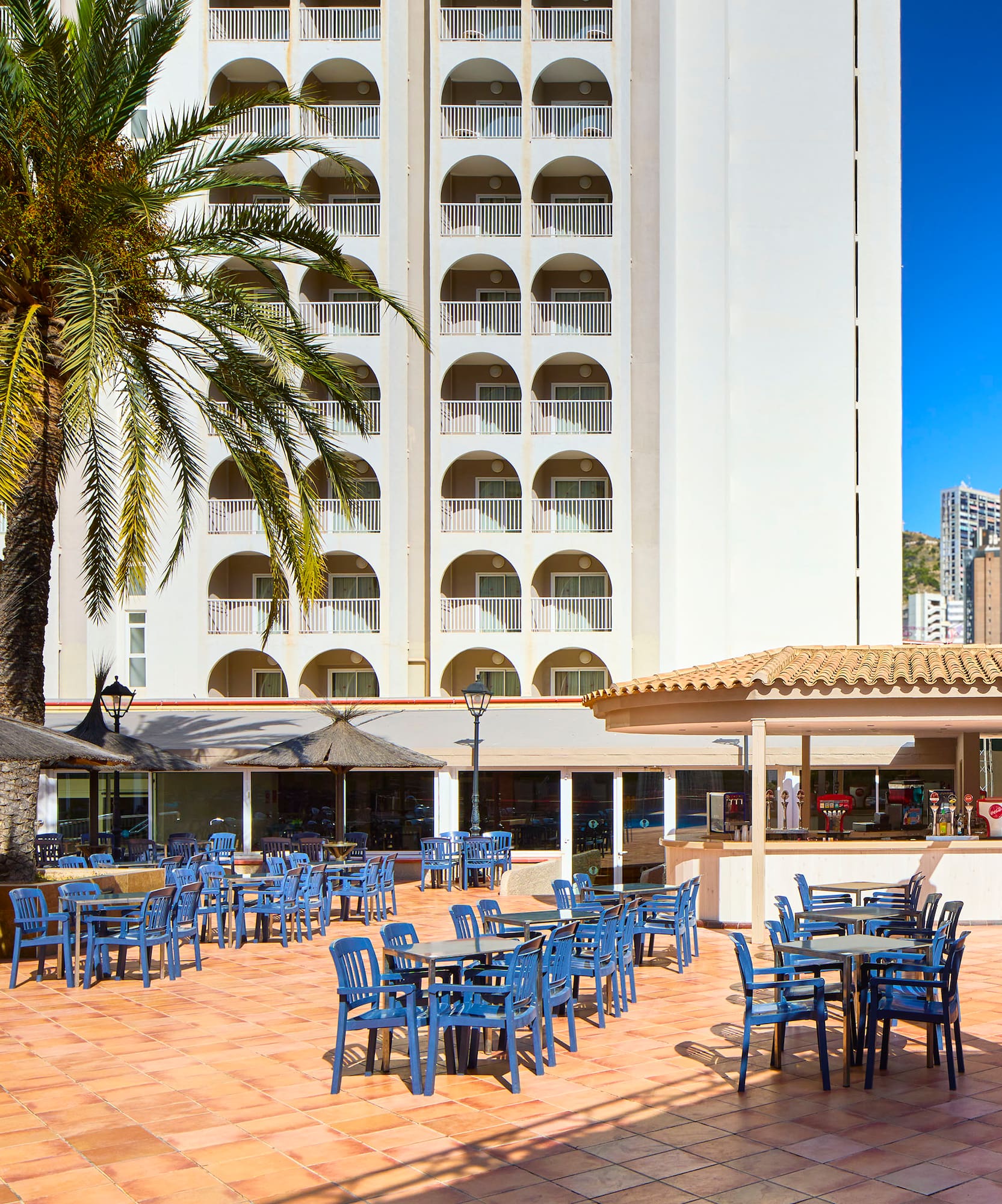 a patio with blue chairs and tables in front of a building