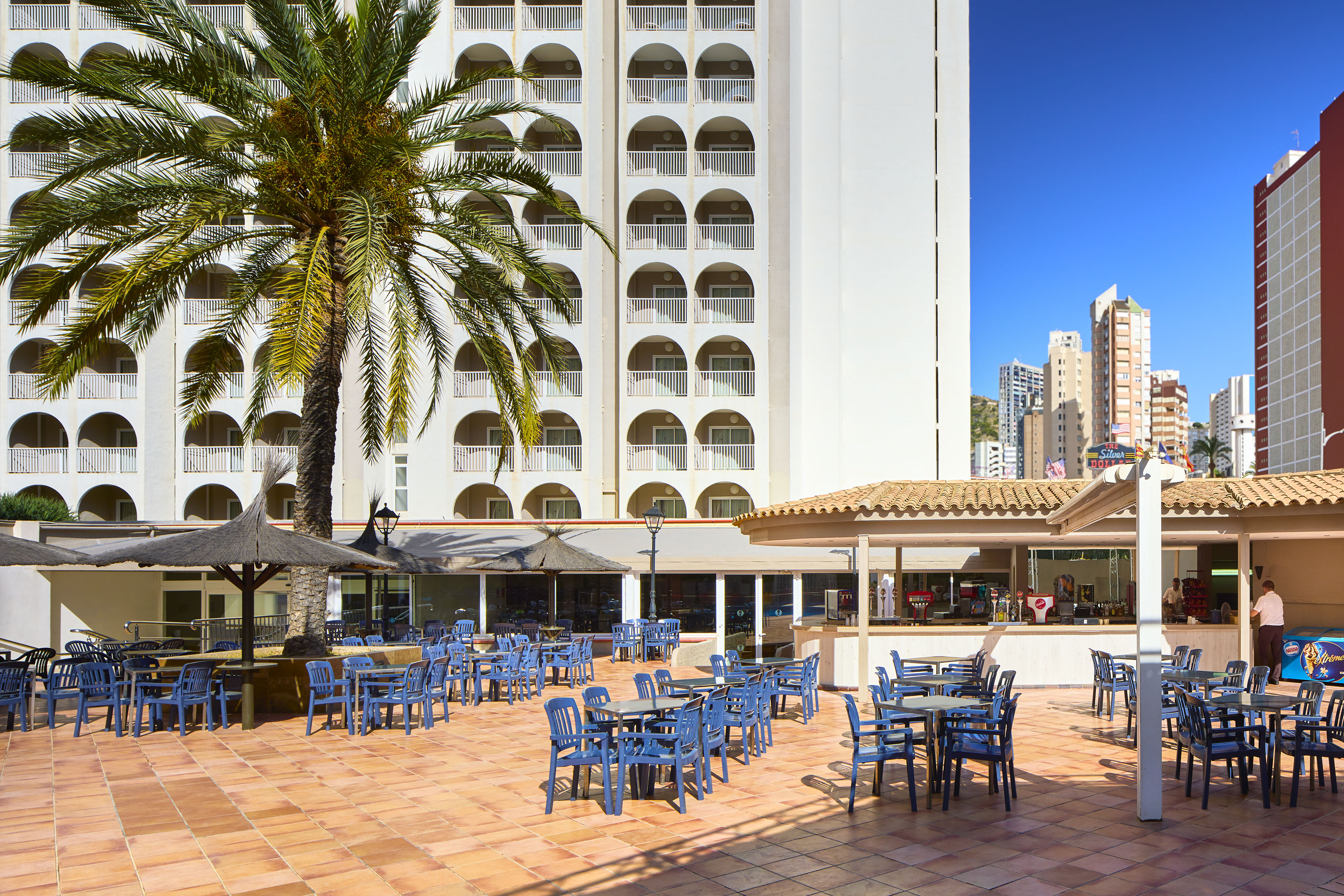 a patio with blue chairs and tables in front of a building