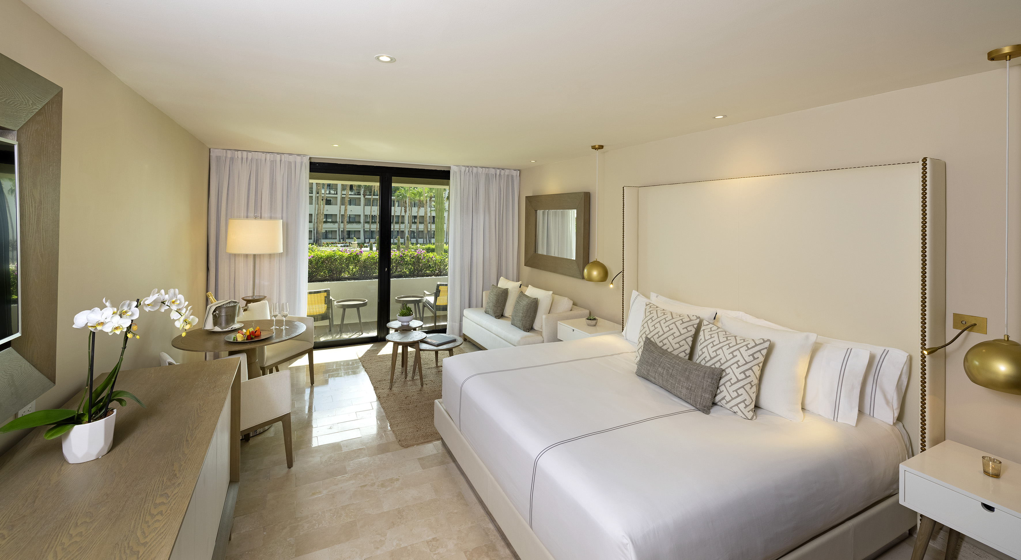 Modern hotel suite with king bed, private balcony, sitting area, and dining table.